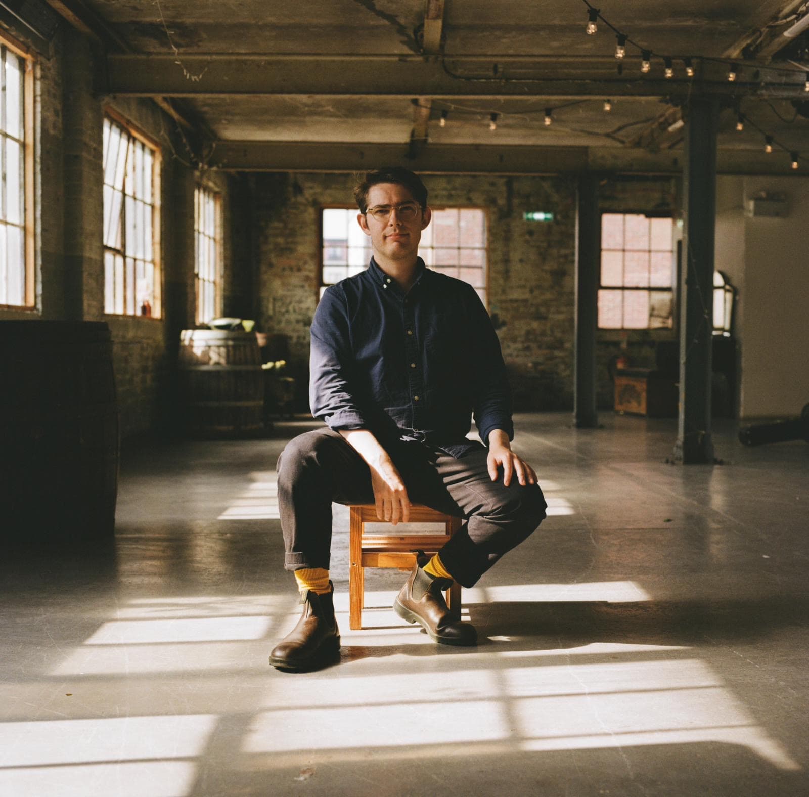 Campbell David Parker seated on a stool in a sunlit industrial space
