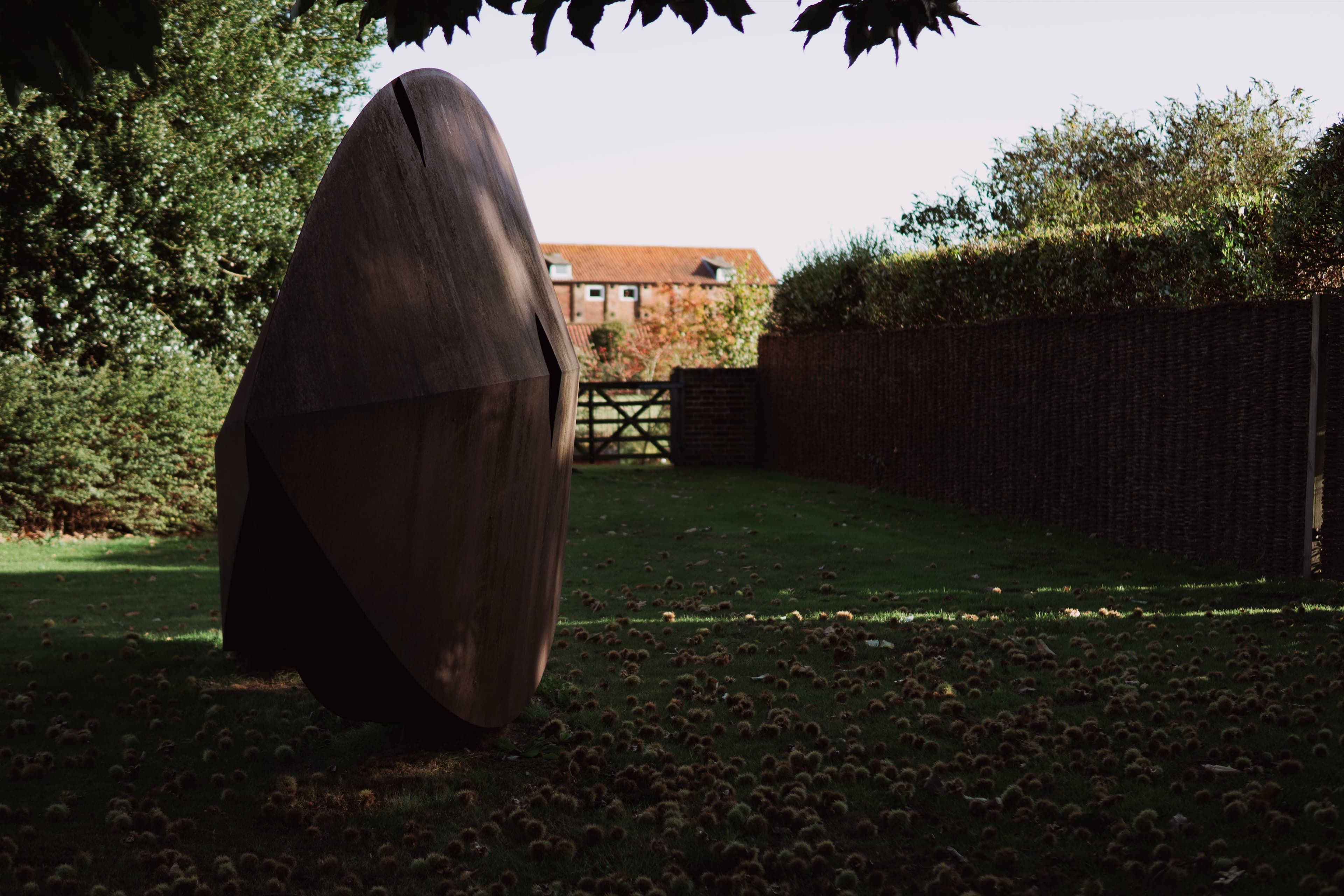 Large abstract stone sculpture in a walled garden with a country house beyond