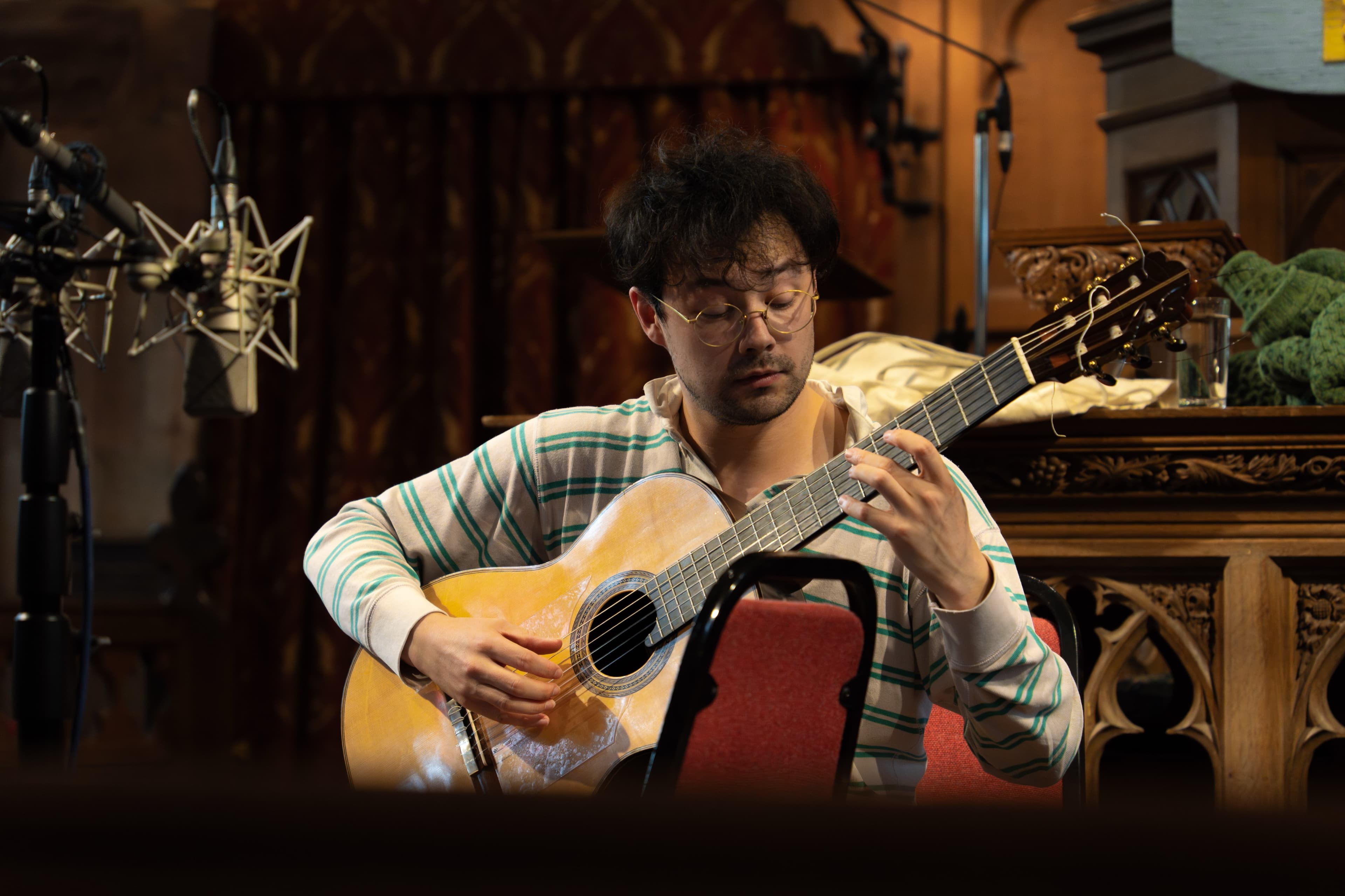 A guitarist playing acoustic guitar during a recording session in an ornate wood-panelled room
