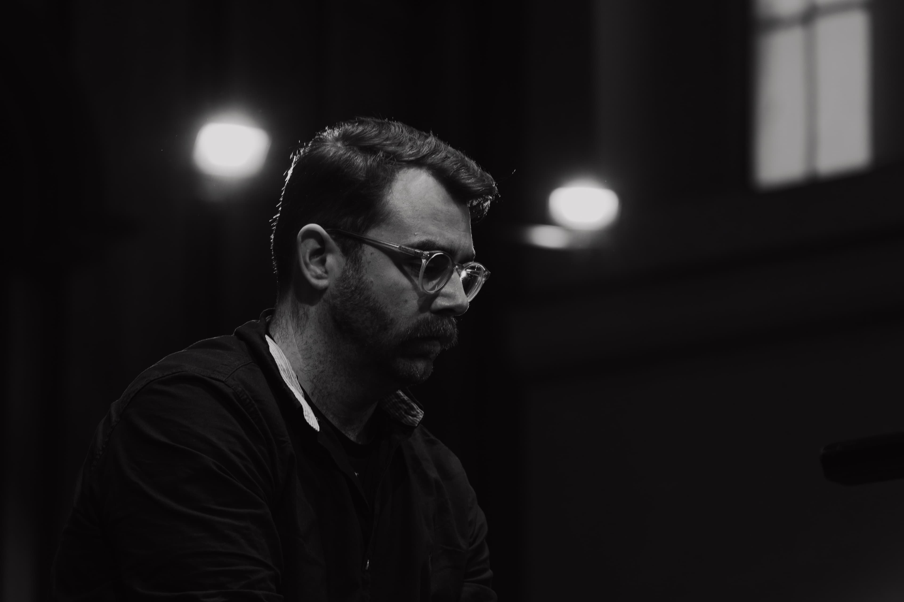A profile portrait of a man lit by stage lights in a rehearsal hall, black and white
