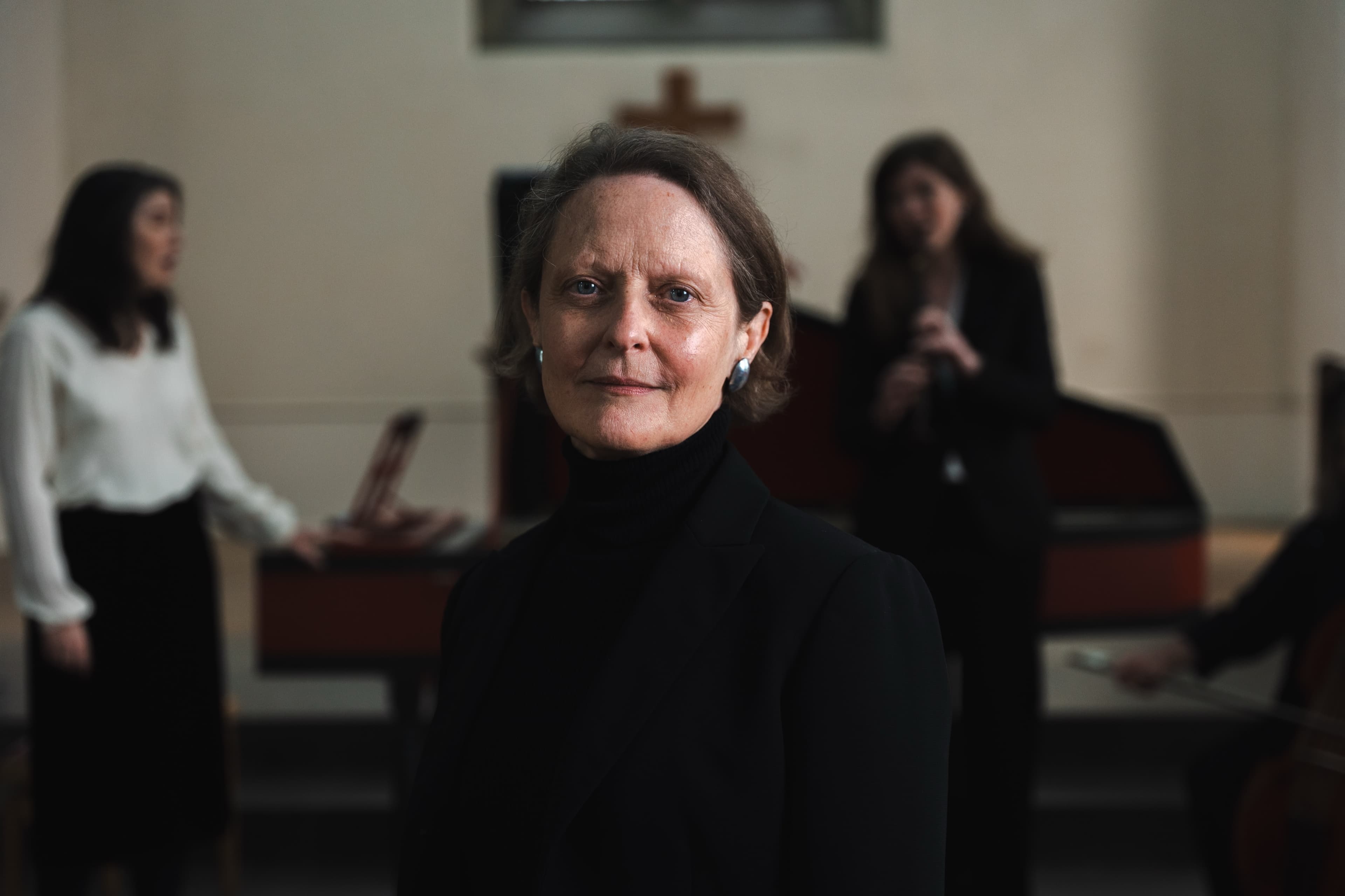 A dramatic portrait of a woman in black with two musicians blurred behind her in a church