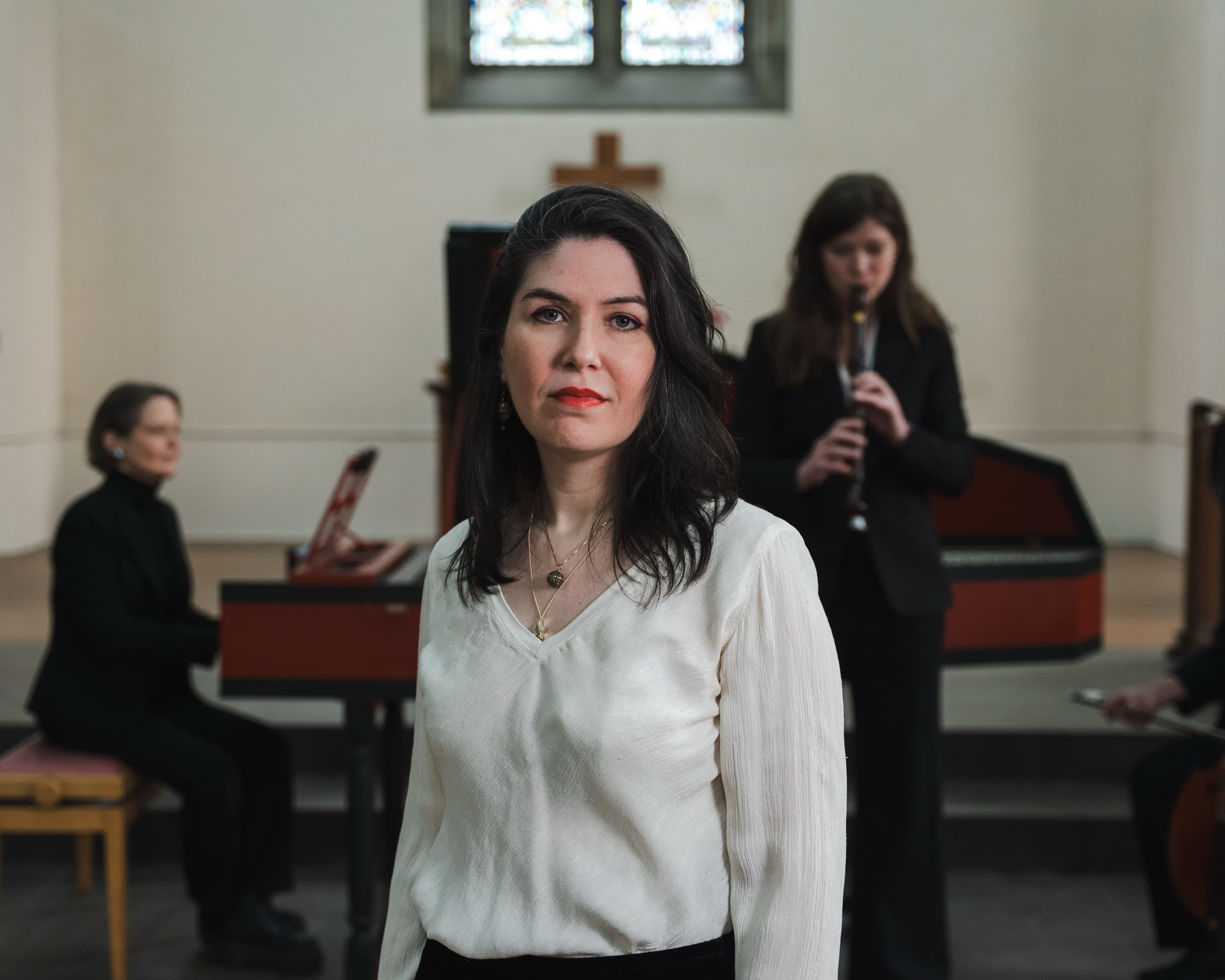 A portrait of a woman in a white blouse with musicians playing recorder and cello blurred behind her