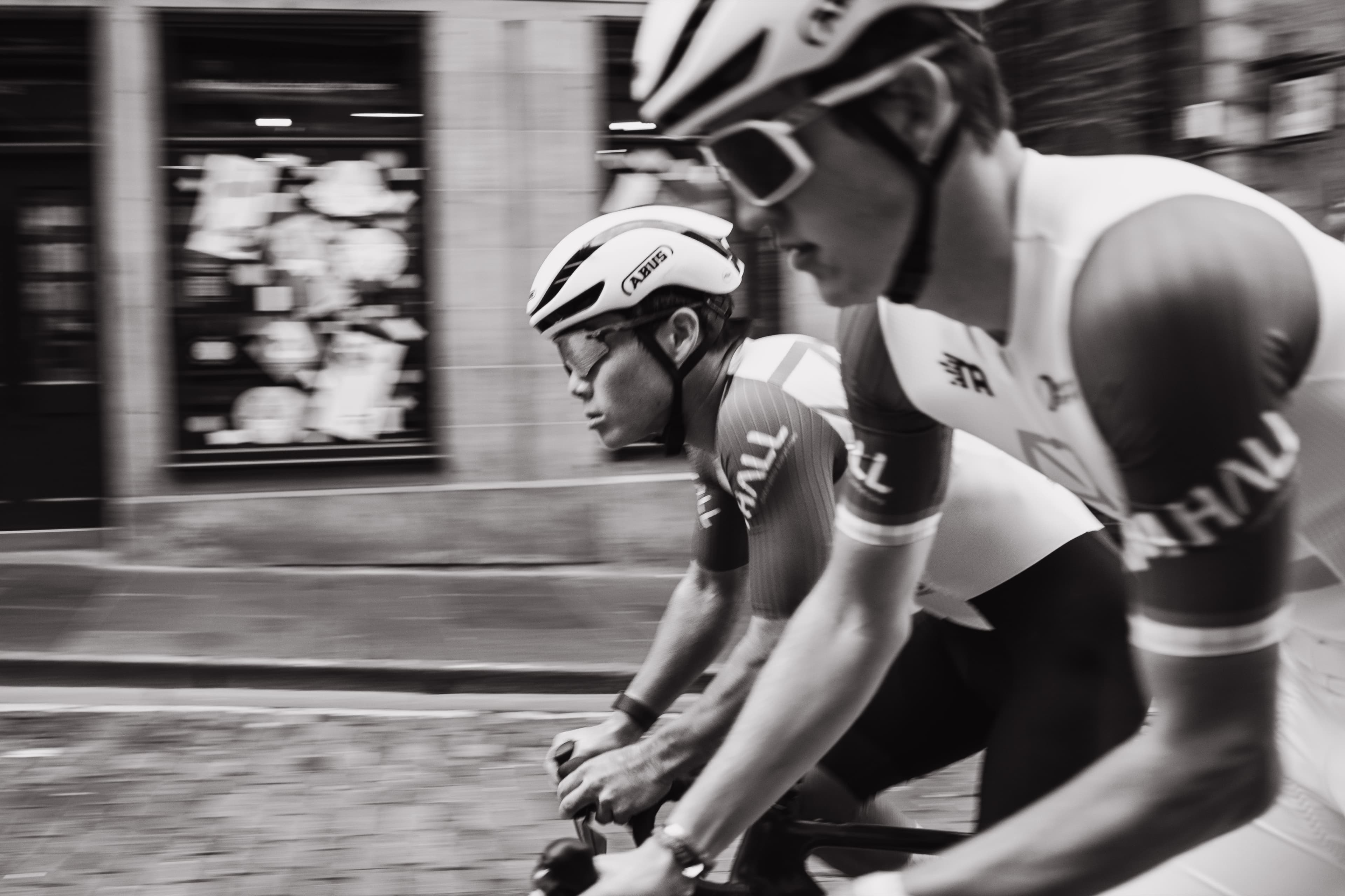 A close, motion-blurred action shot of two cyclists riding, black and white