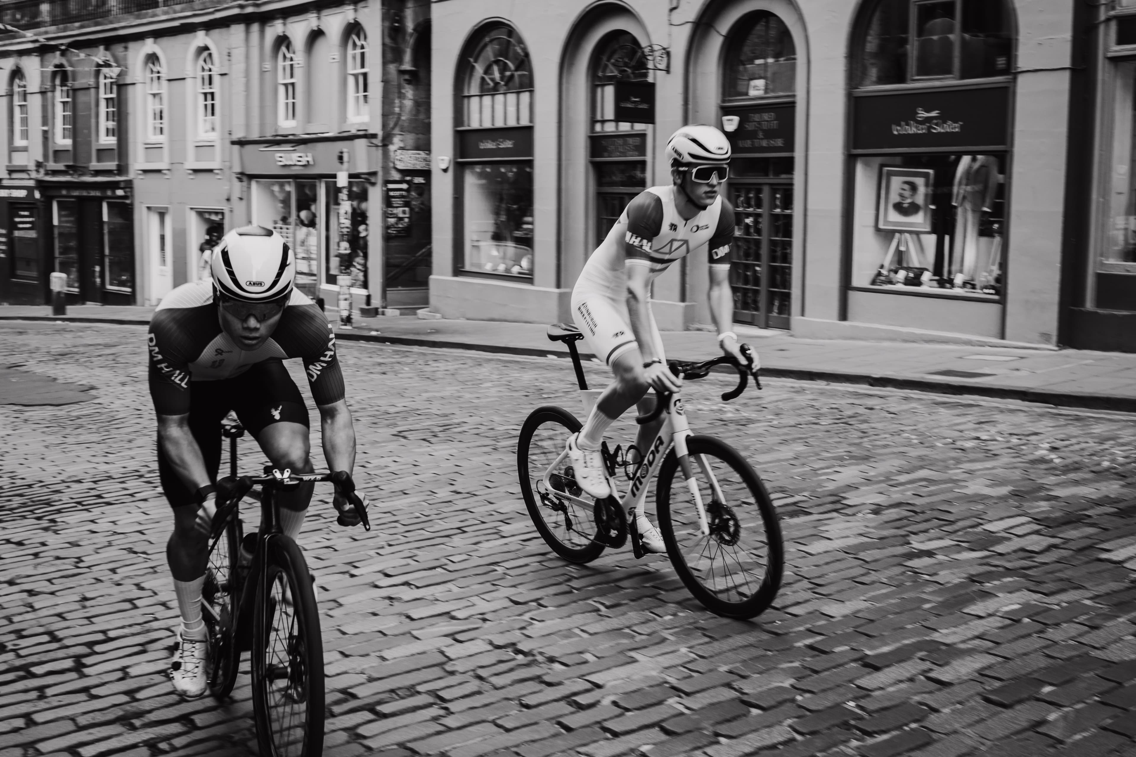 Two cyclists riding fast over cobblestones, black and white