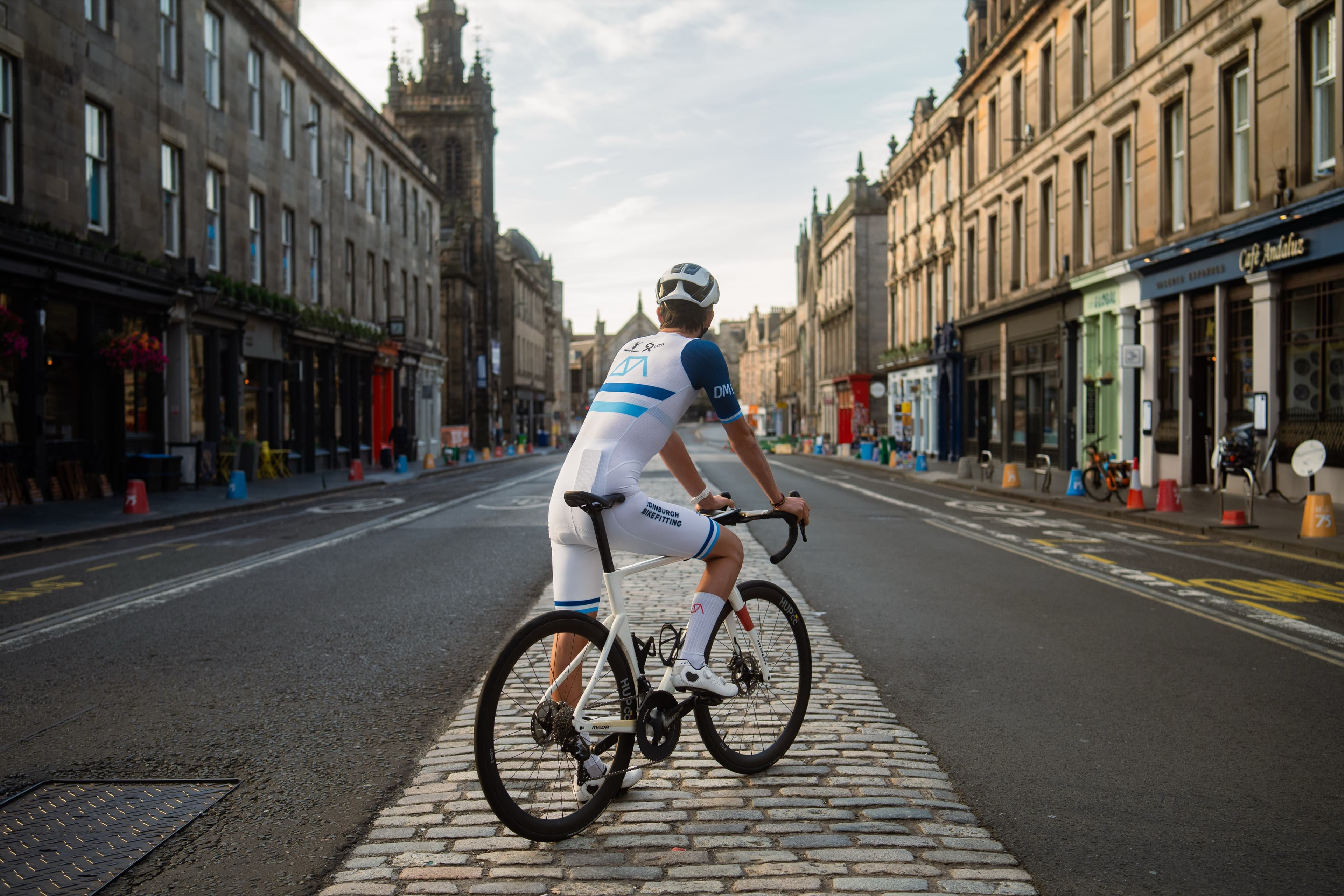 A cyclist stopped on a cobbled Edinburgh street in golden hour light