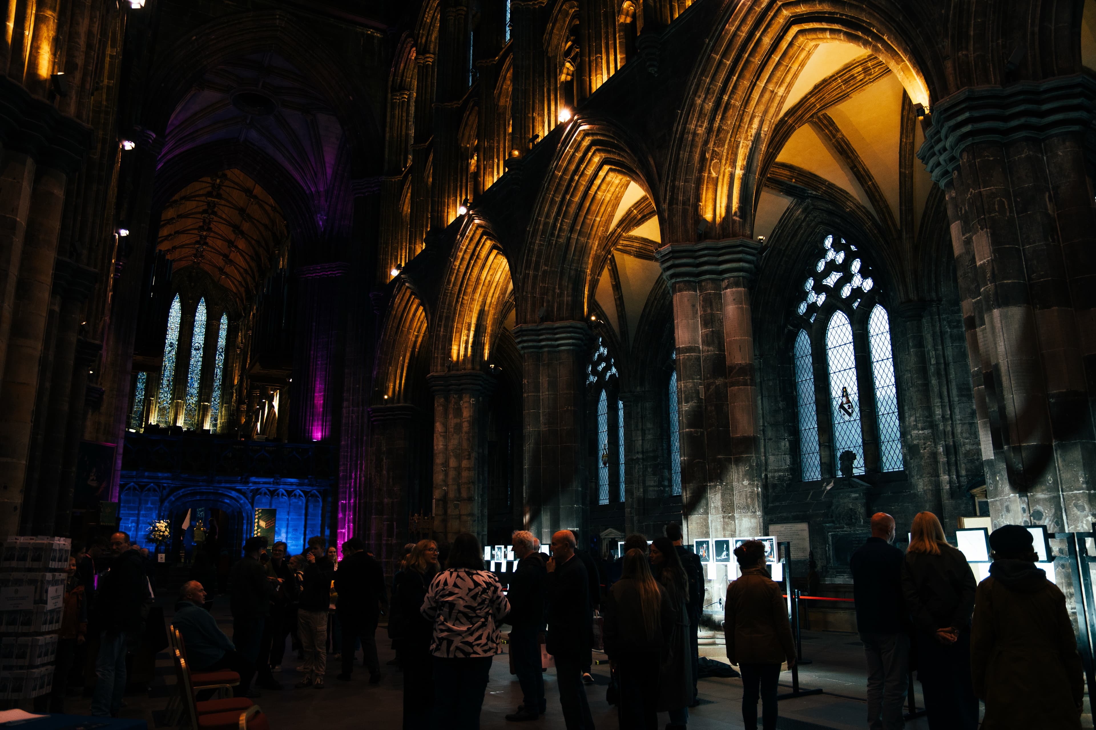 A crowd browsing an illuminated exhibition display beneath gold-lit gothic arches in a cathedral