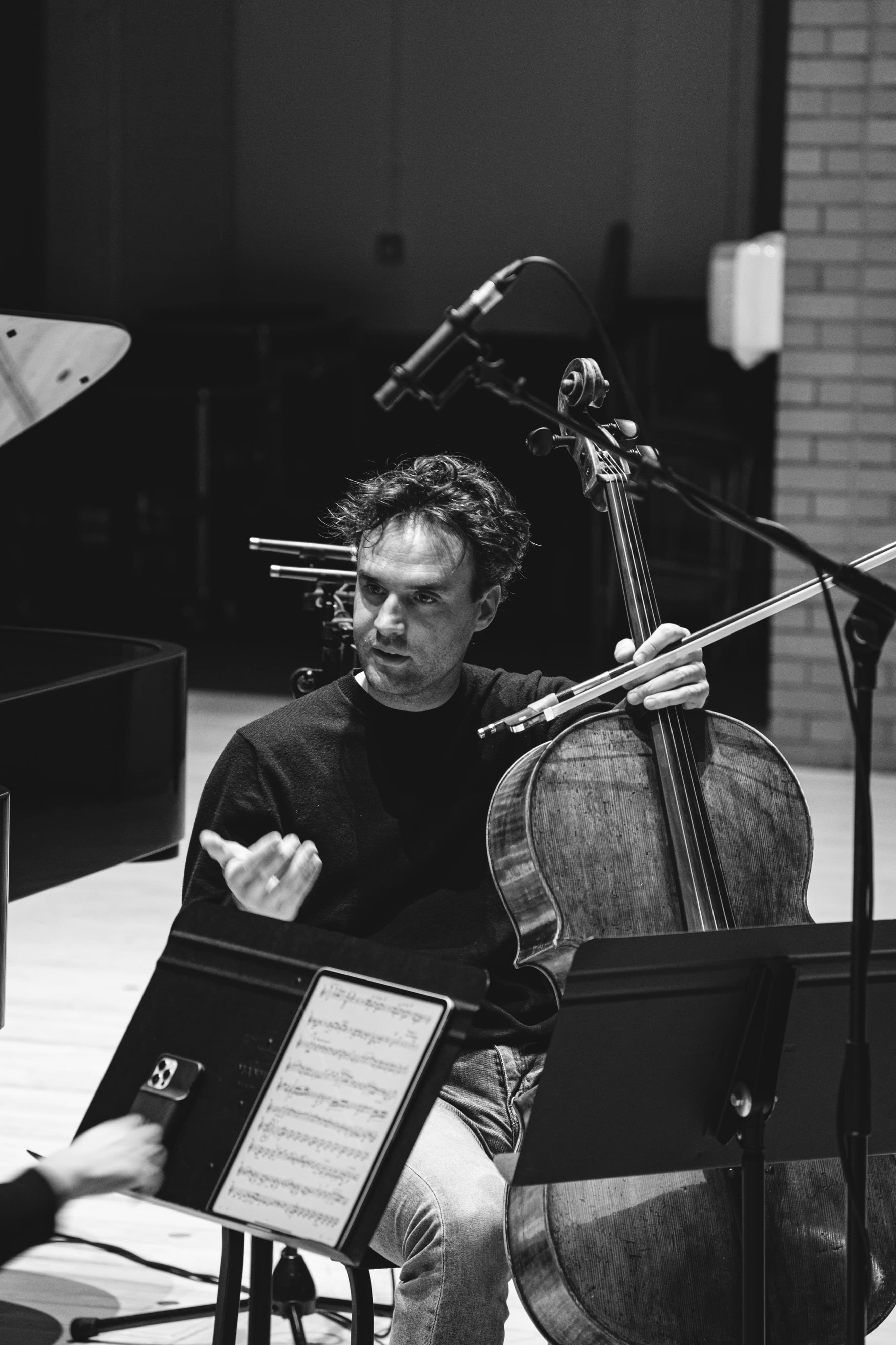 A cellist gesturing mid-conversation while holding a cello and bow, black and white