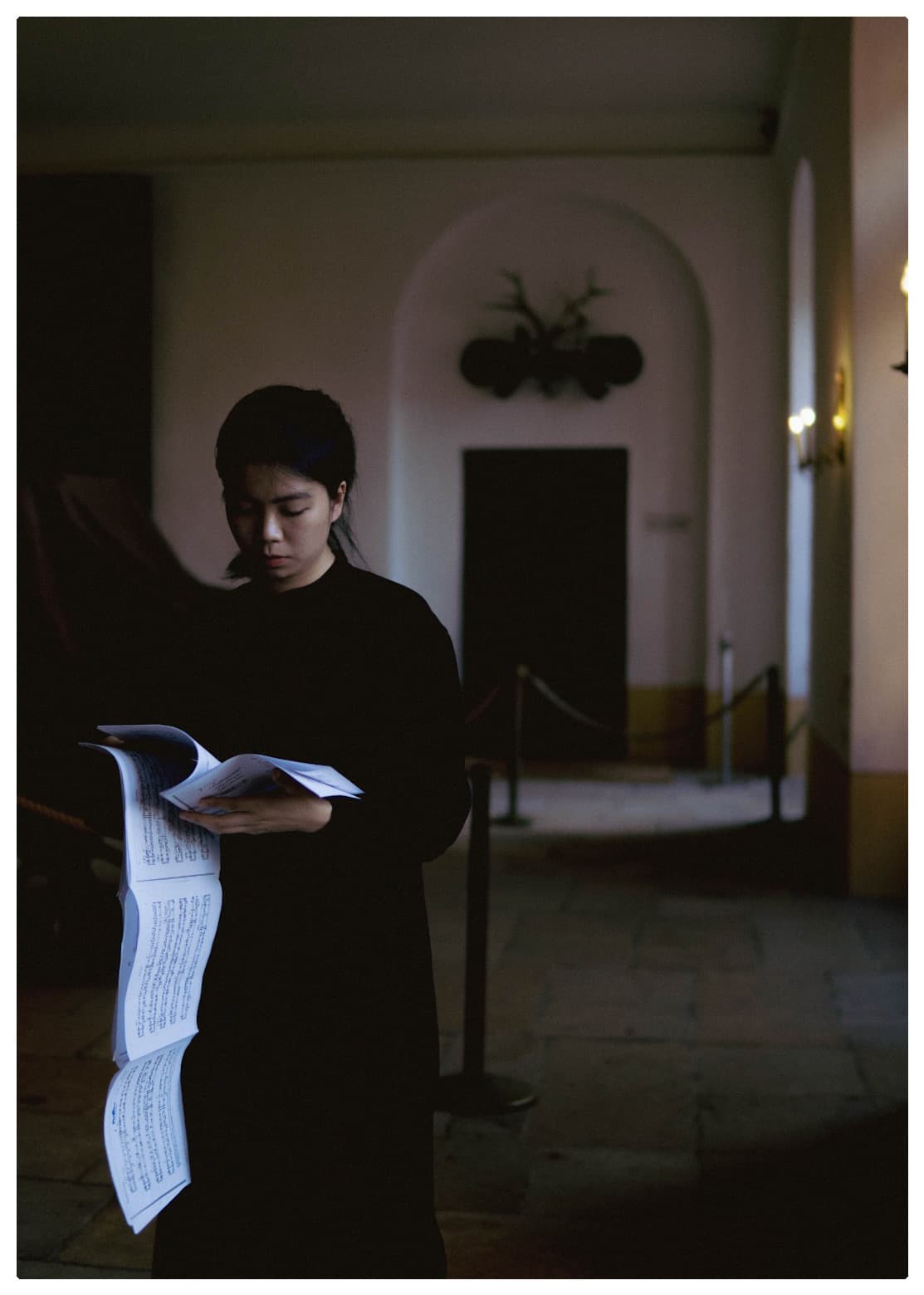 A woman in black reading sheet music in a dimly lit historic interior