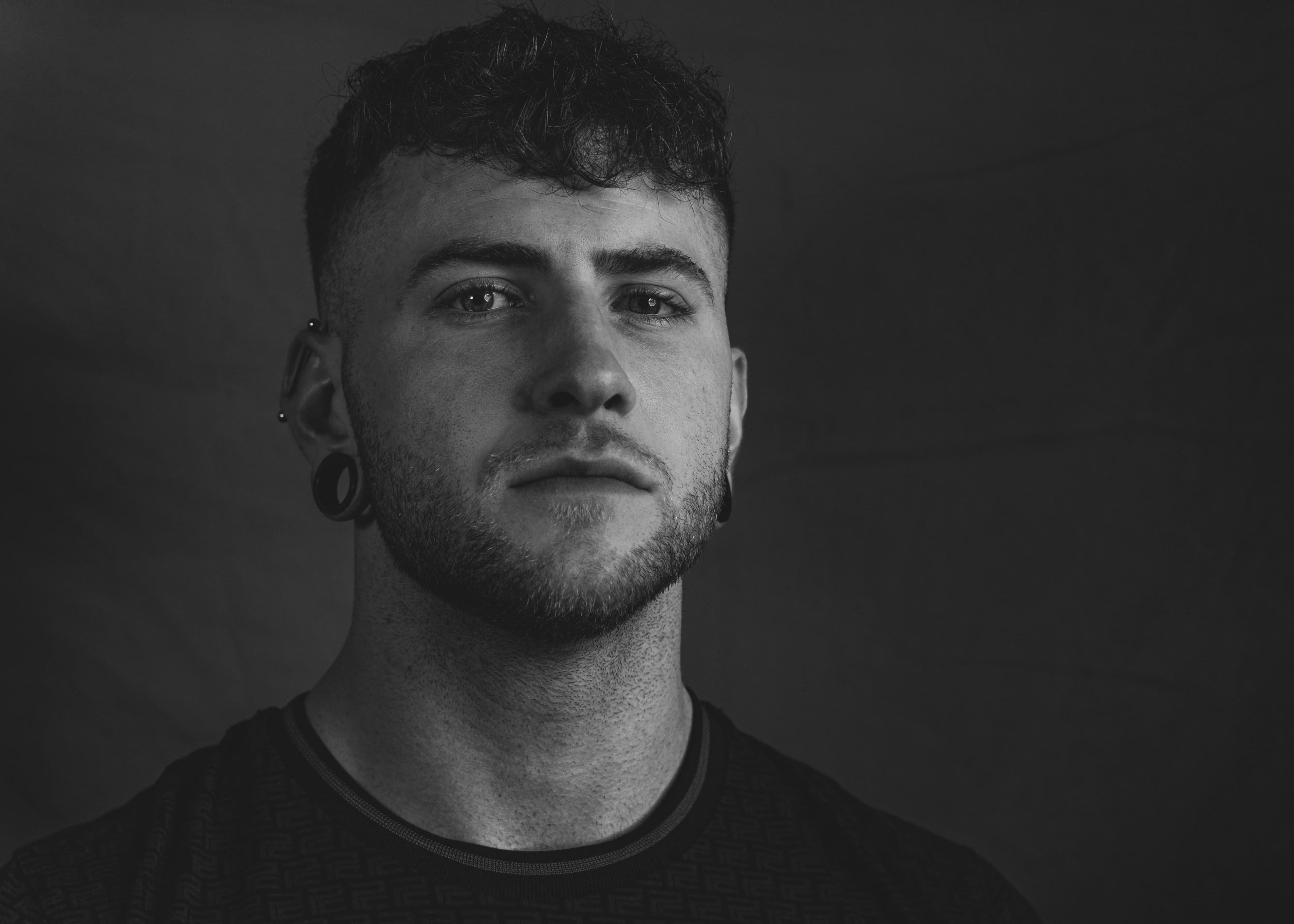 A black and white close-up portrait of a man with curly hair and ear piercings