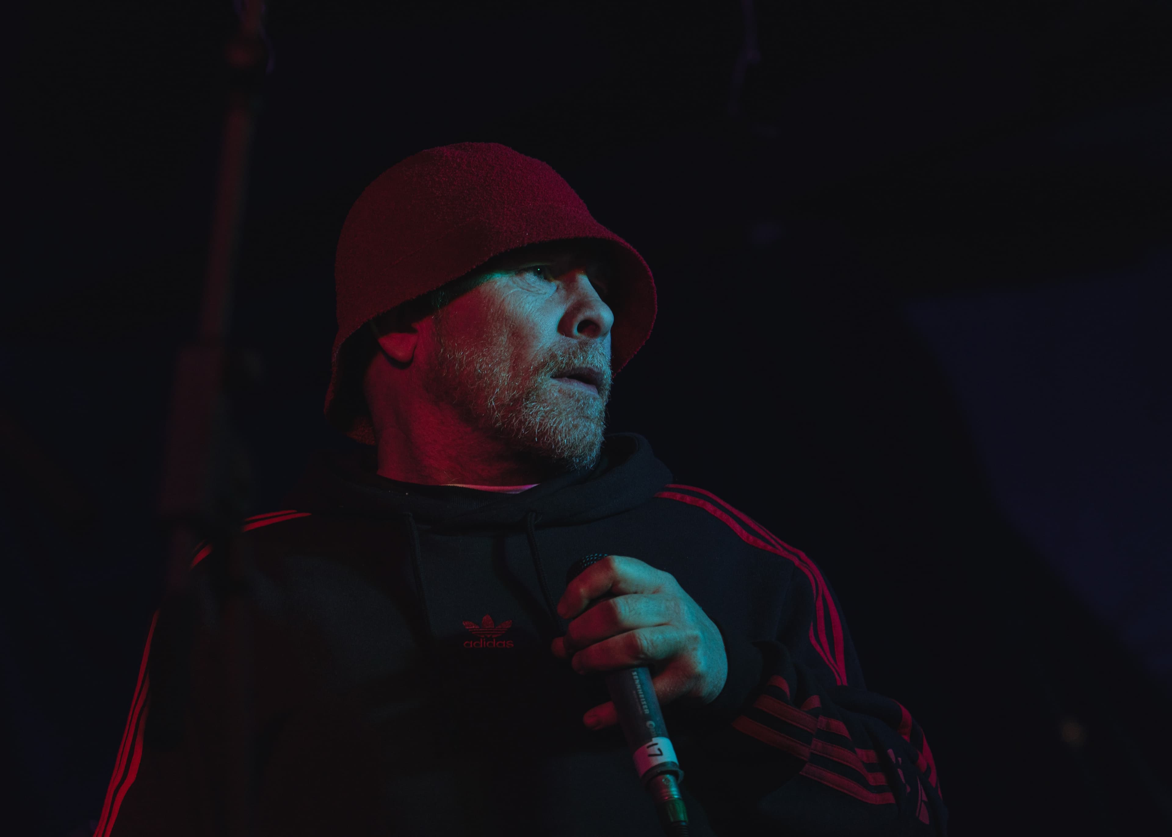 A performer in a red bucket hat and striped hoodie holding a microphone under red and blue lighting