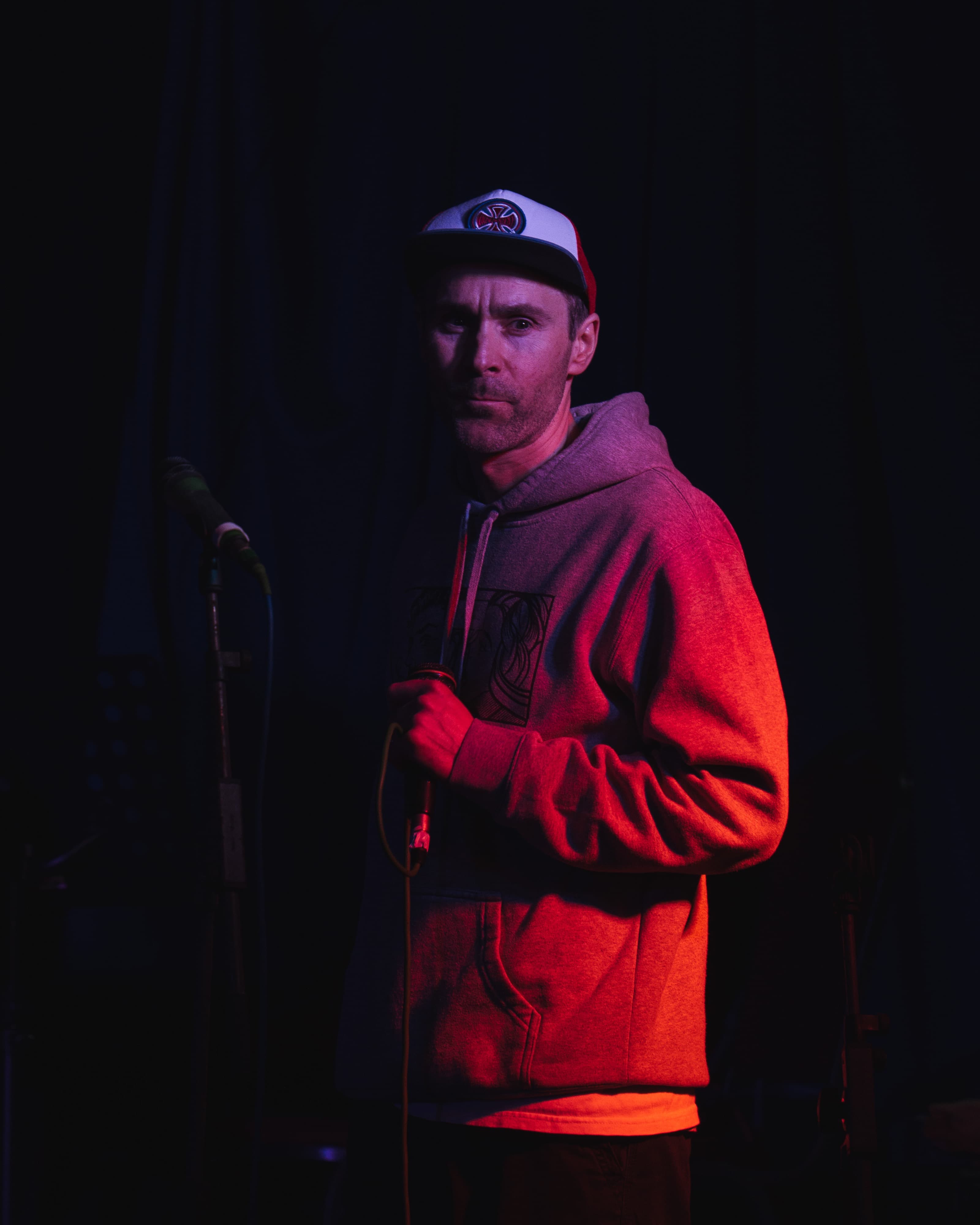 A performer in a cap holding a microphone under red stage lighting