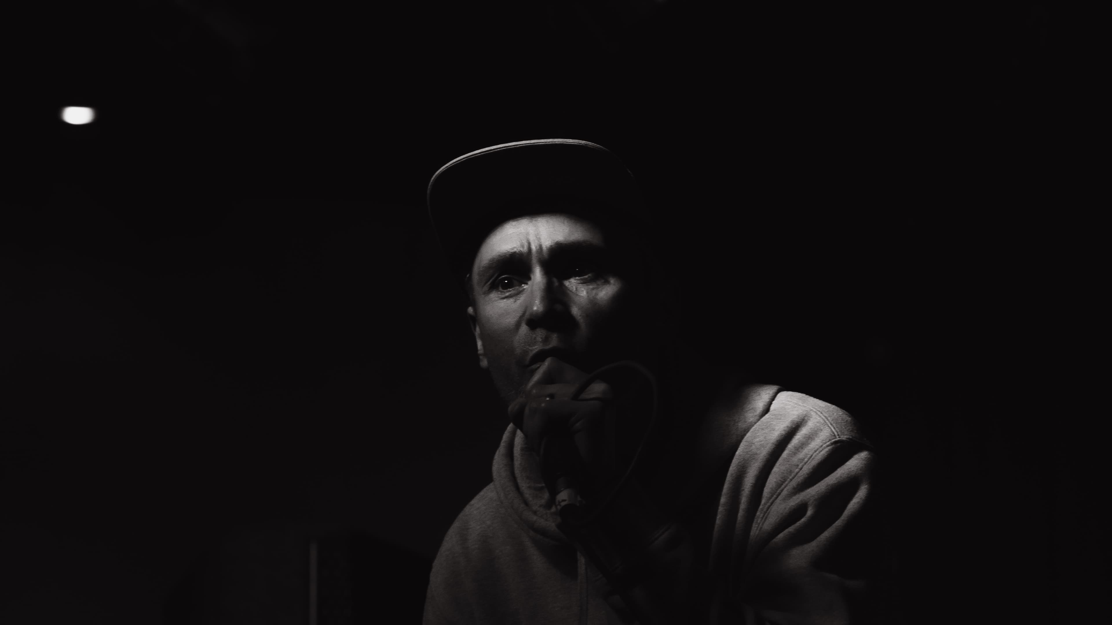 A performer in a cap speaking closely into a microphone, black and white