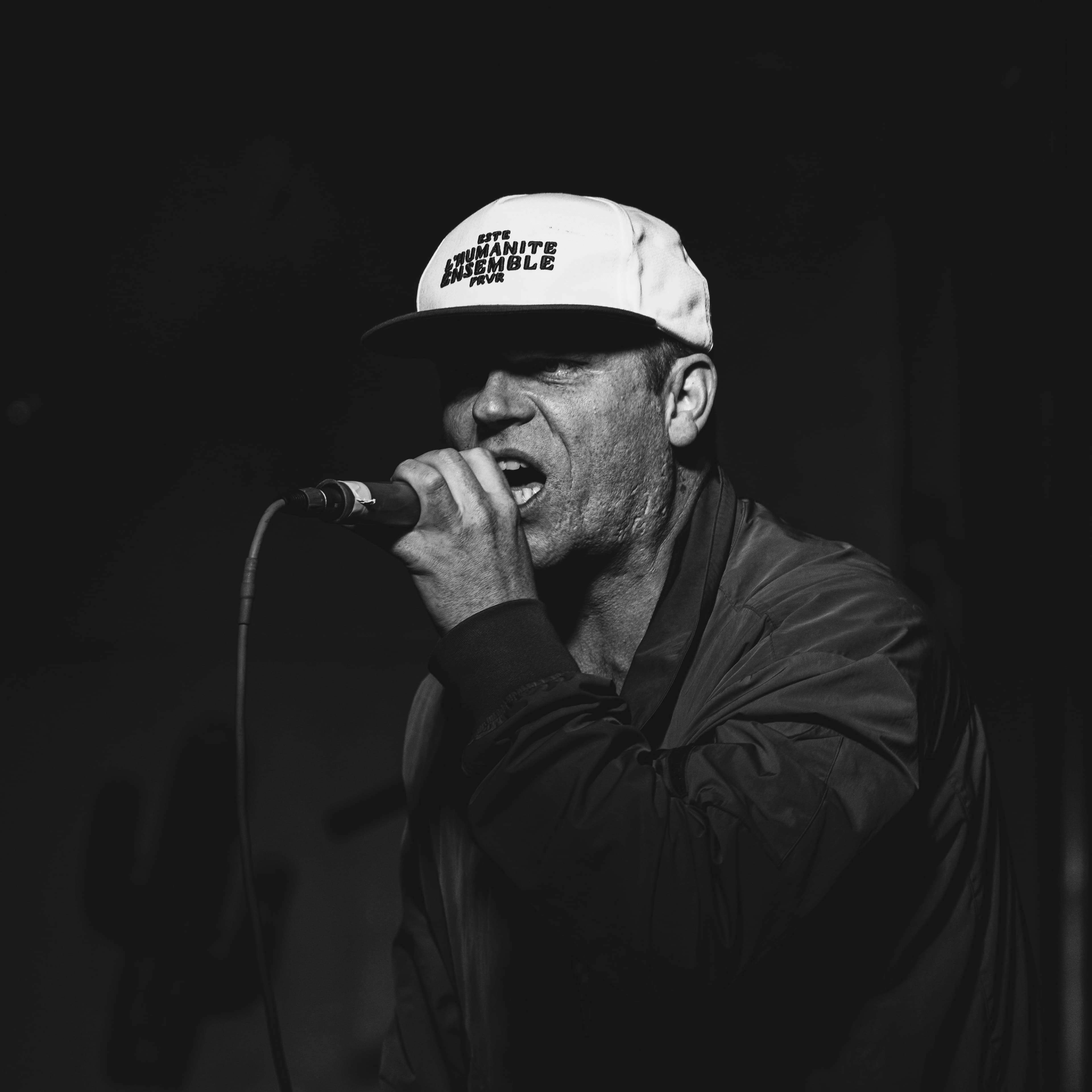 A performer wearing a graphic t-shirt singing into a microphone, black and white