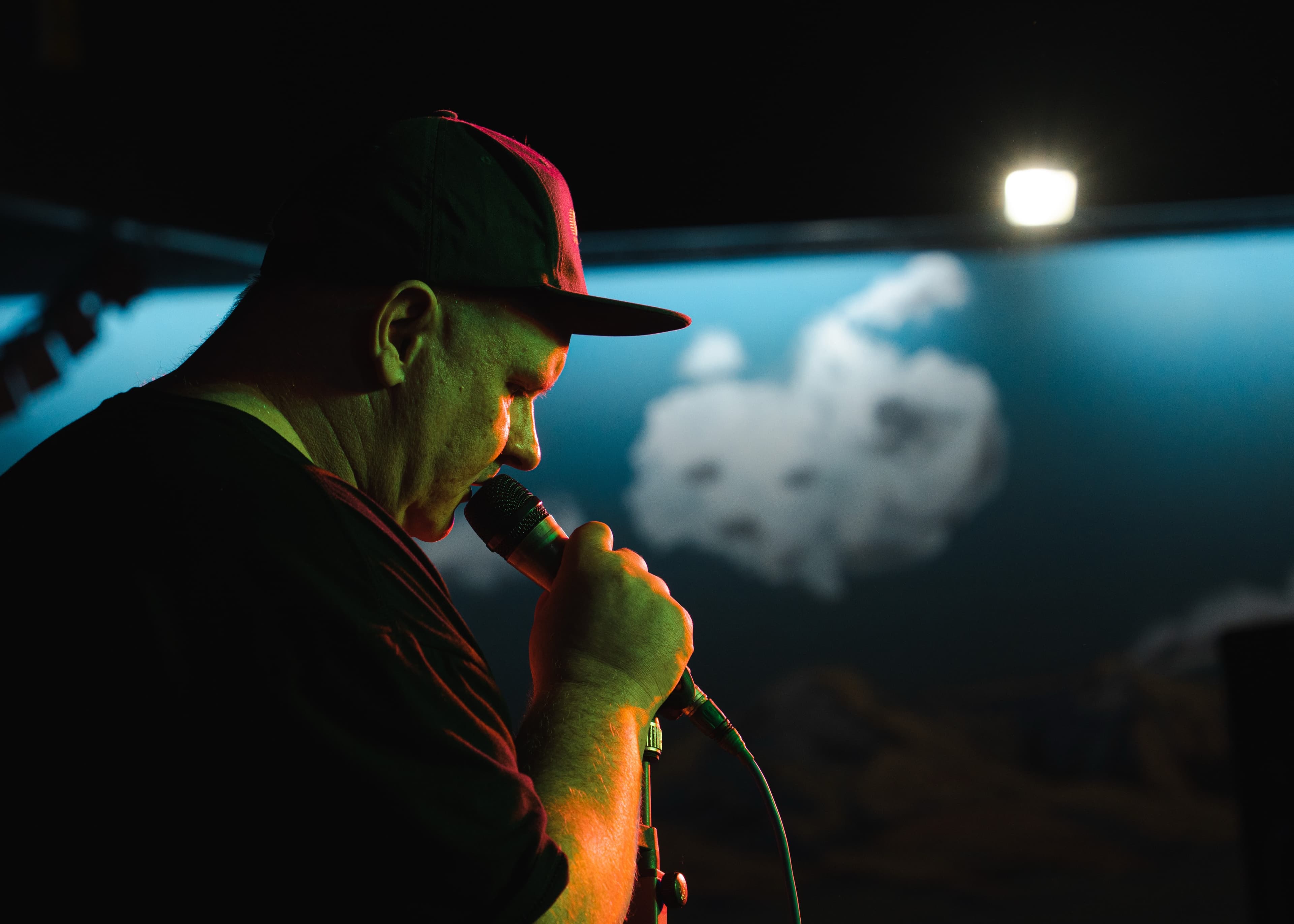 A performer in a cap singing into a microphone in profile, black and white
