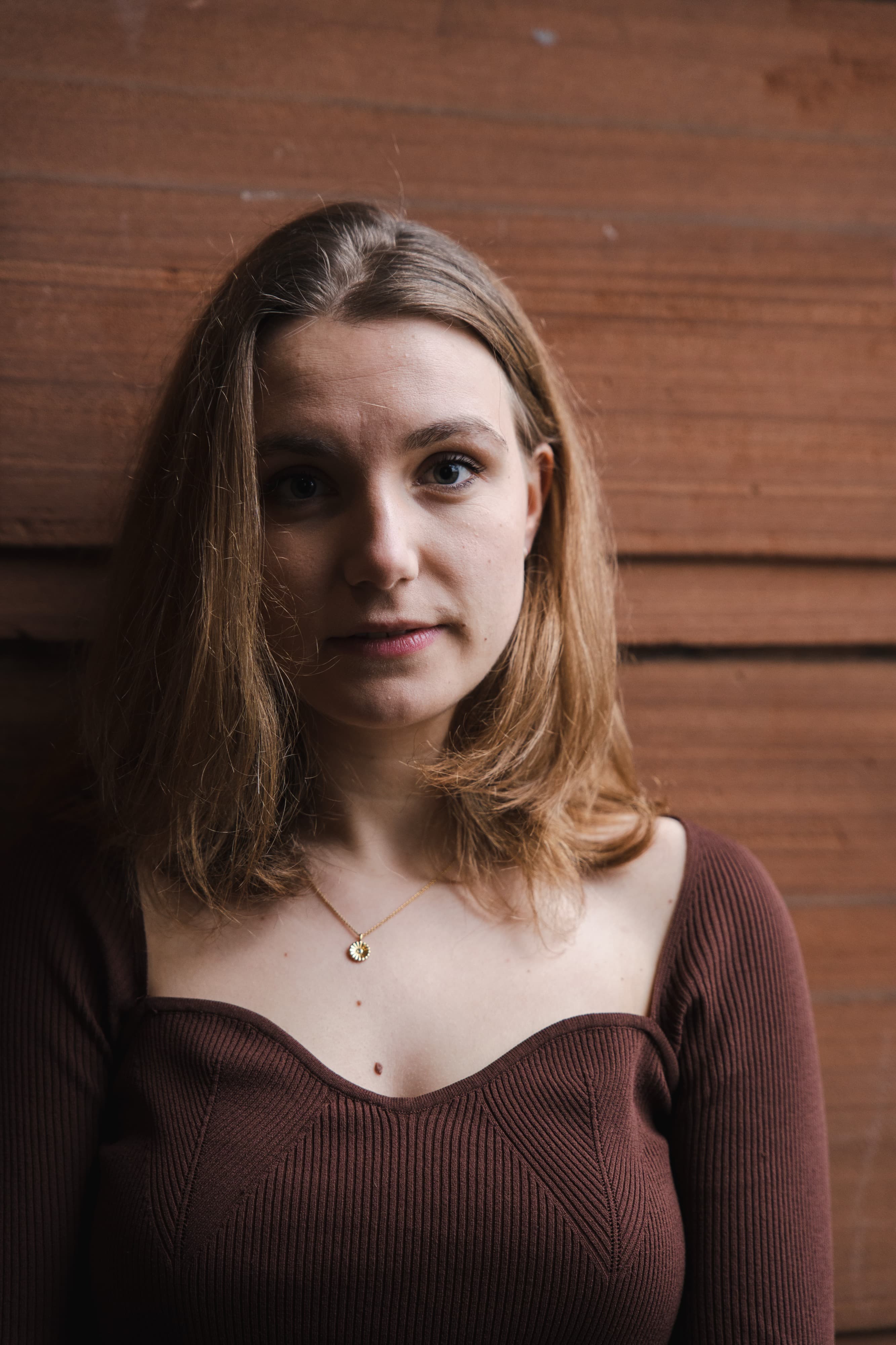 A portrait of a woman with light brown hair against a wooden wall