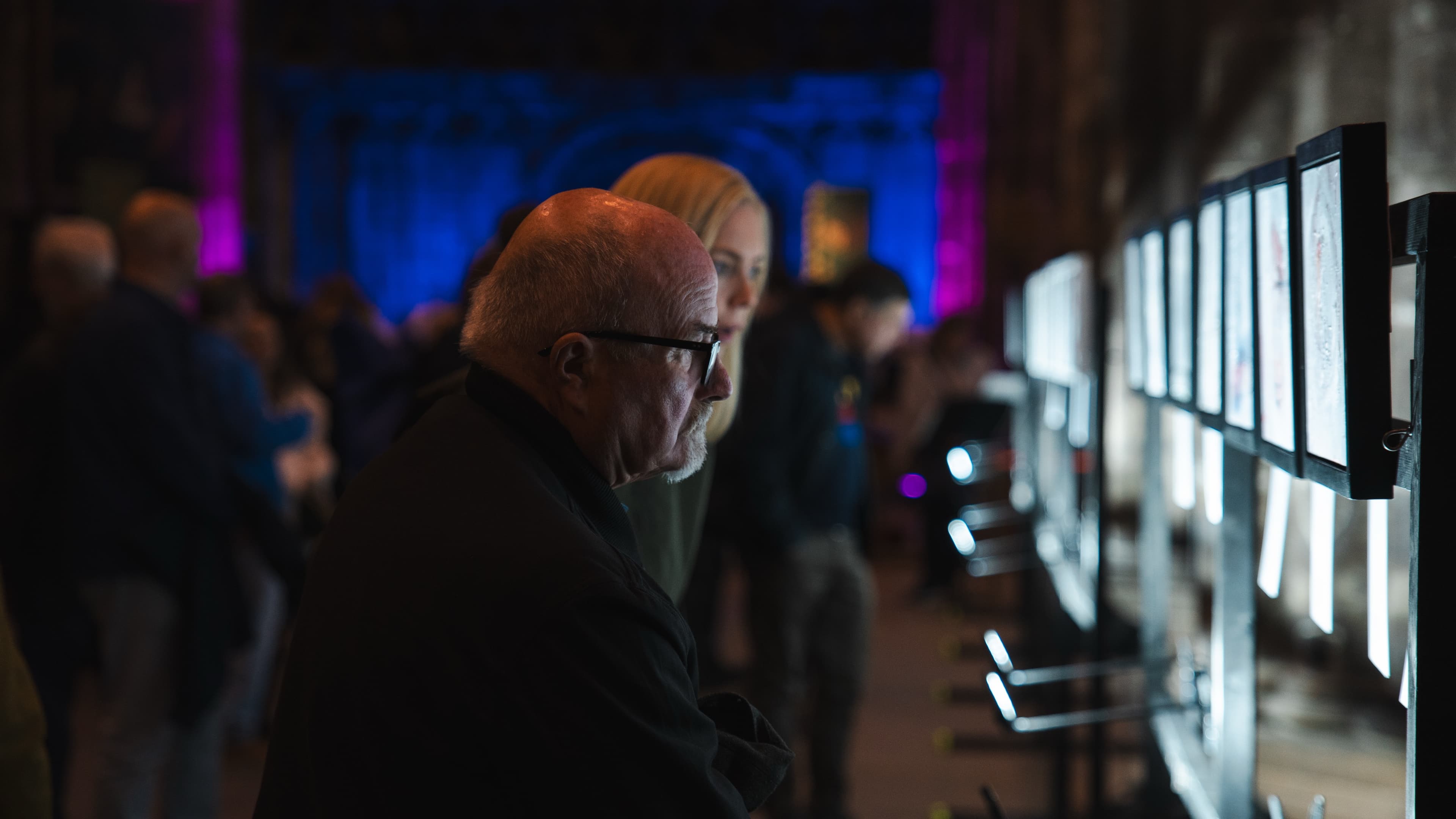 A man in profile studying an illuminated exhibition panel in a dimly lit cathedral