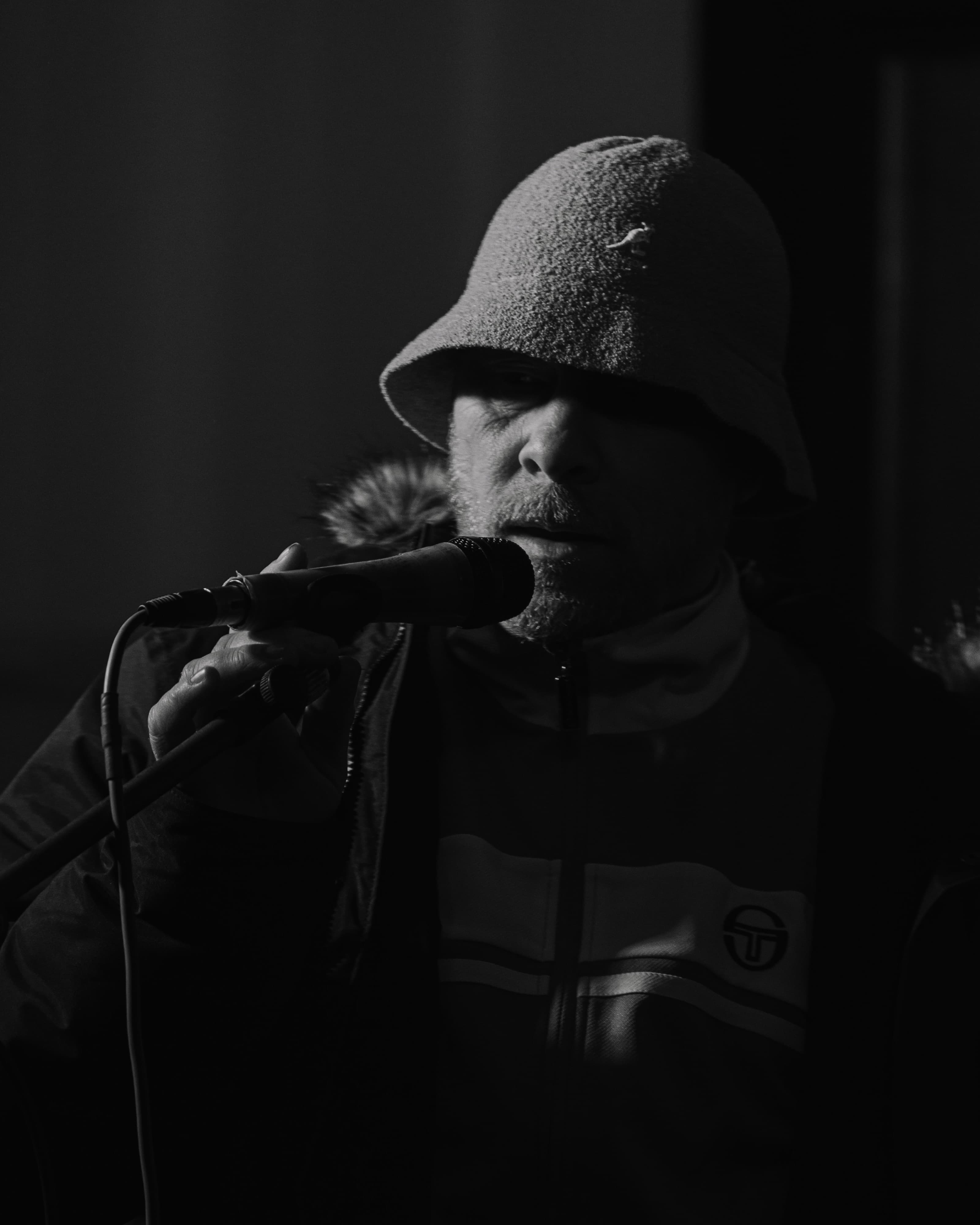 A performer in a bucket hat singing into a microphone, black and white