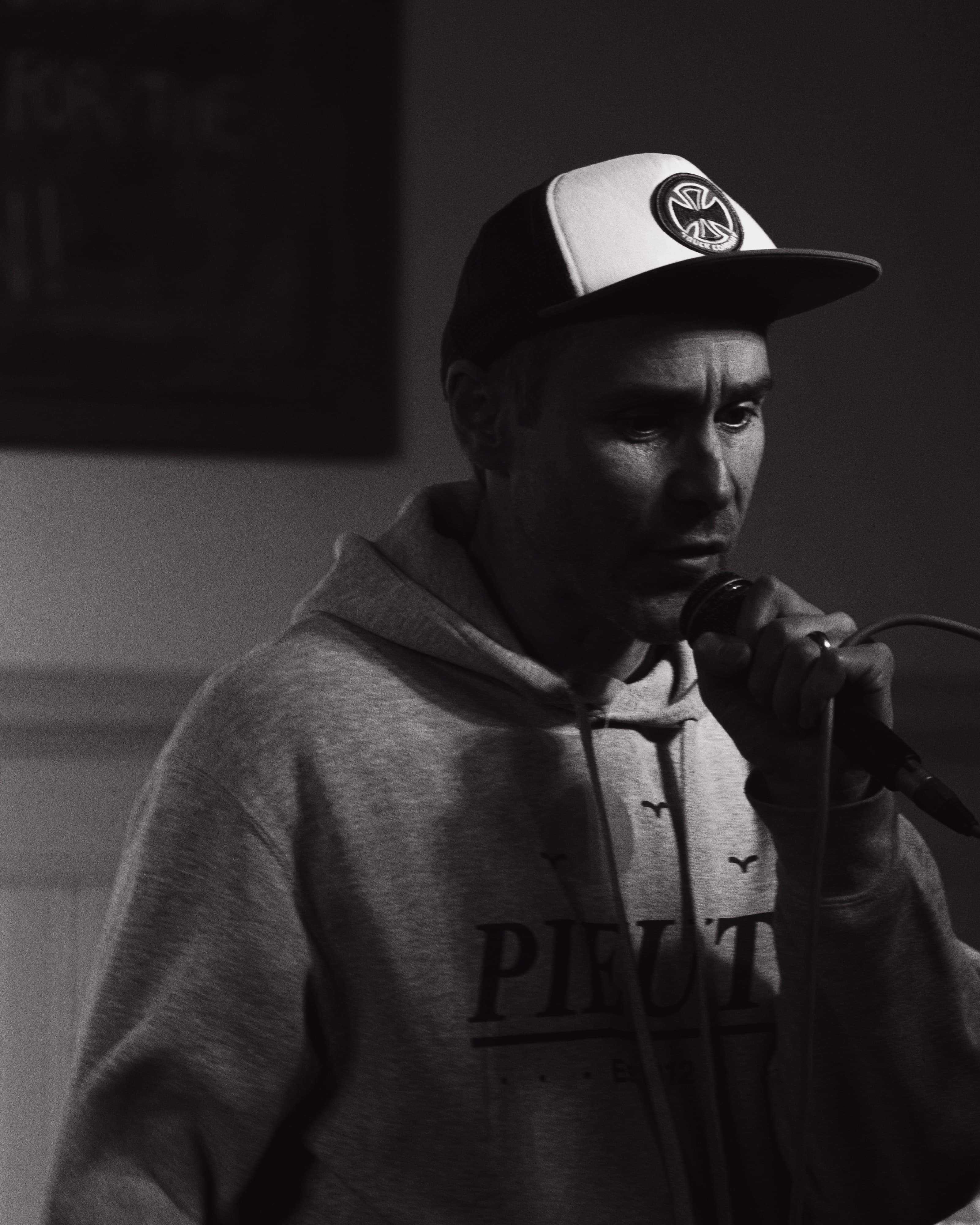 A performer in a cap and hoodie singing into a microphone, black and white