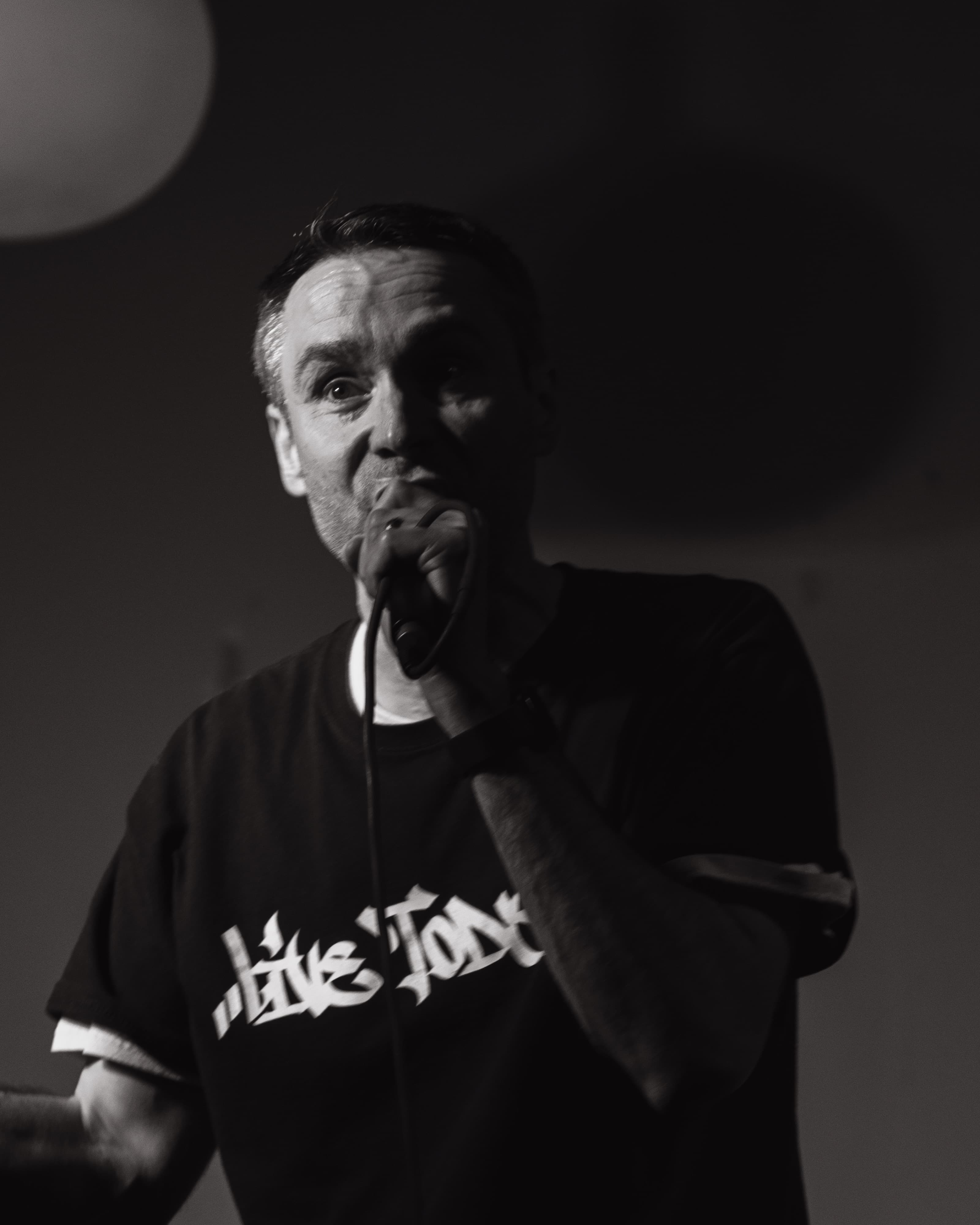 A performer in a trucker cap singing into a microphone, black and white