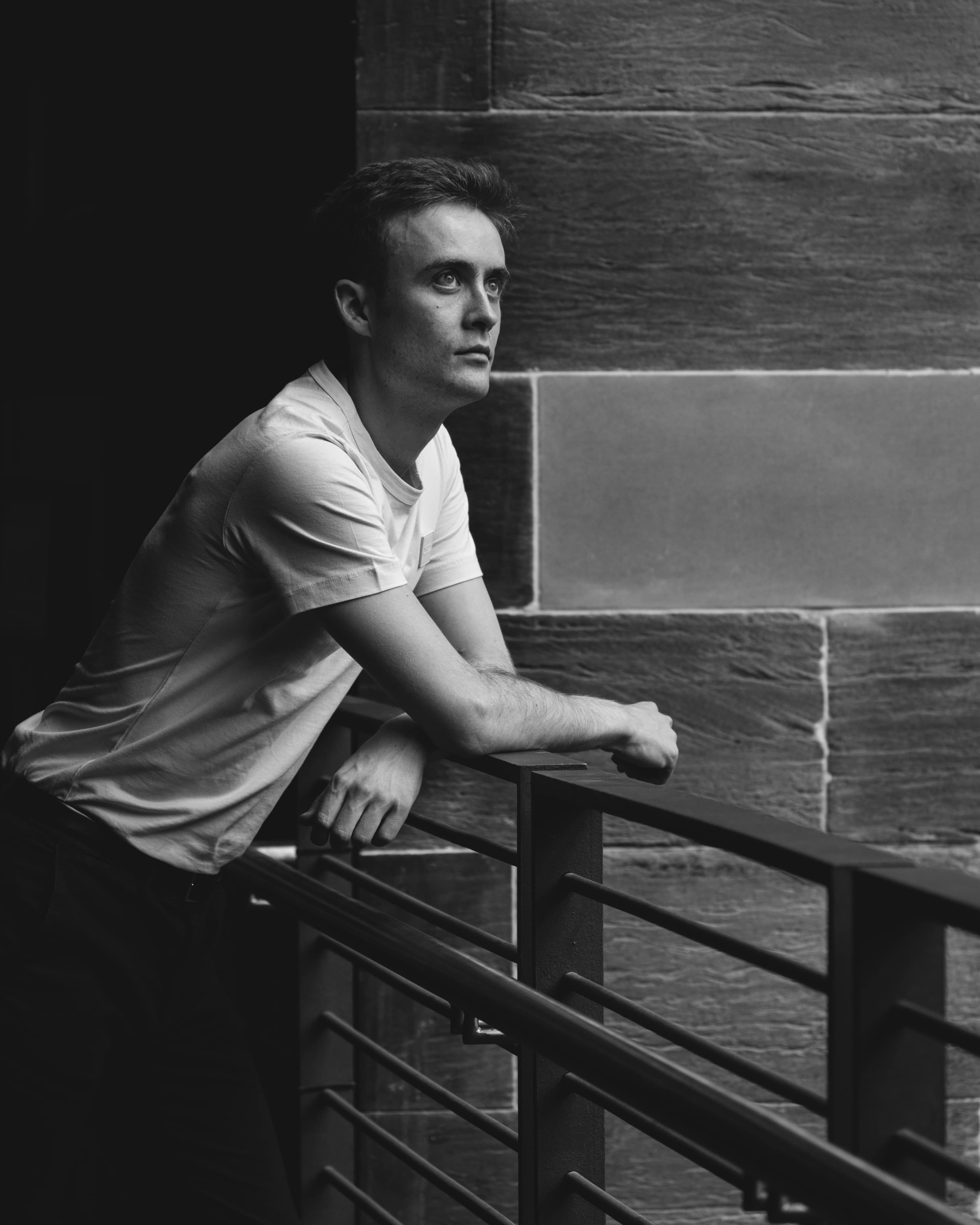 A man leaning on a railing, looking up, black and white portrait