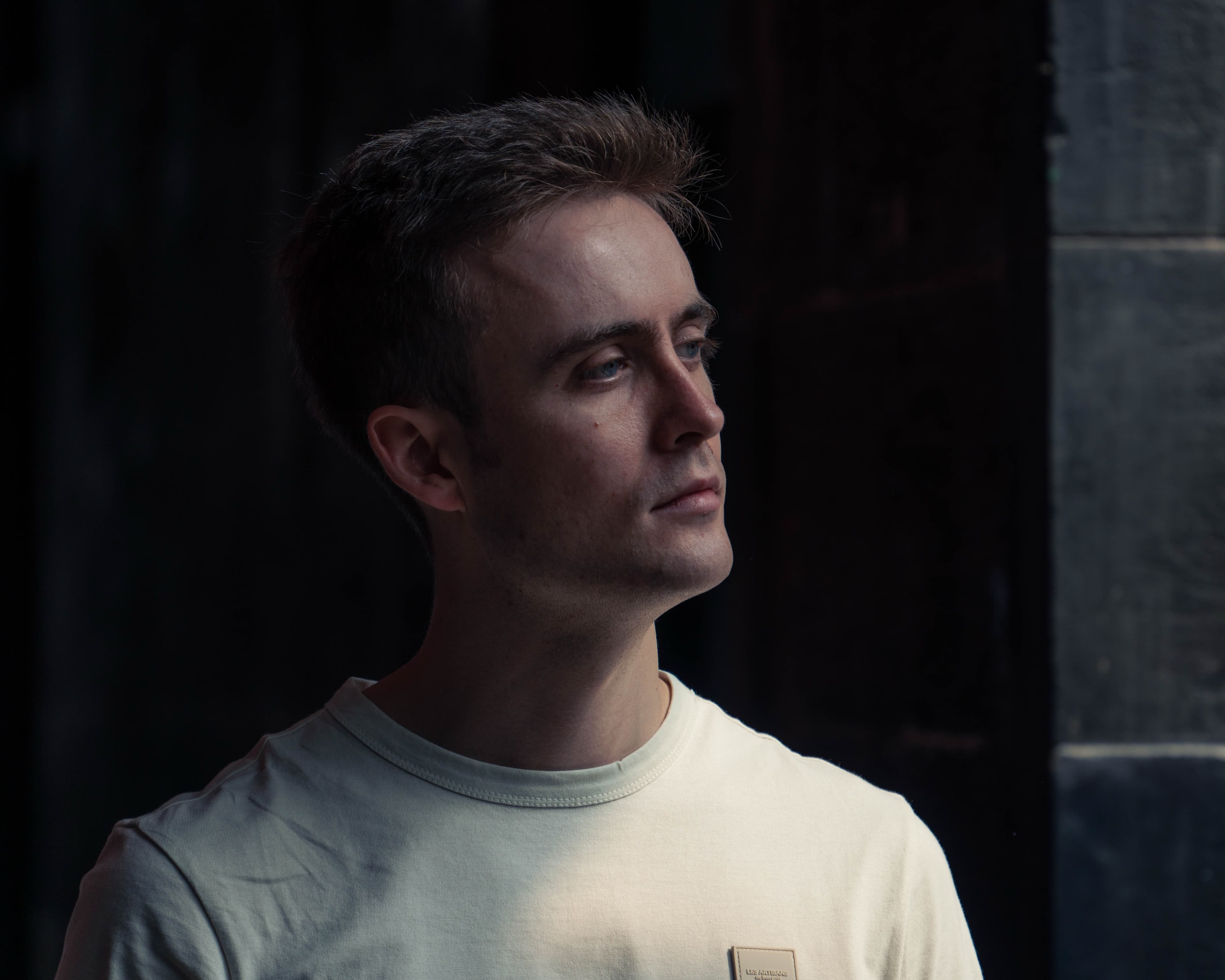 A portrait of a man in a white t-shirt looking off to the side against a dark background