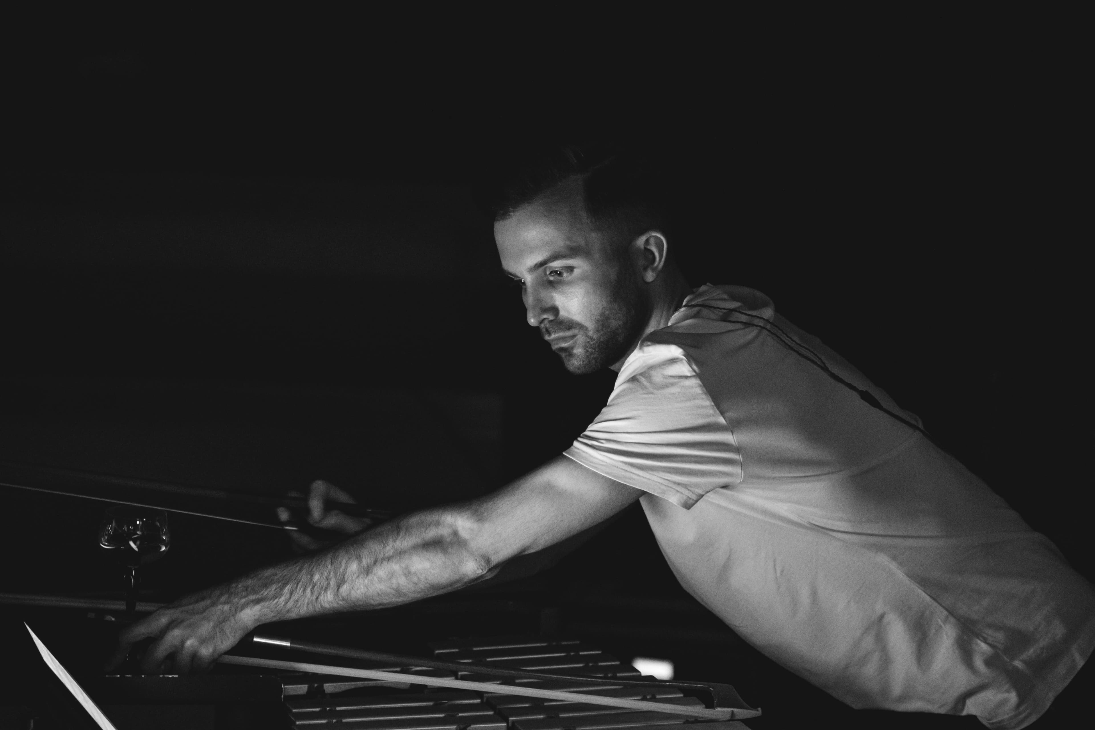 A percussionist reaching across a vibraphone with mallets in a darkened hall, black and white