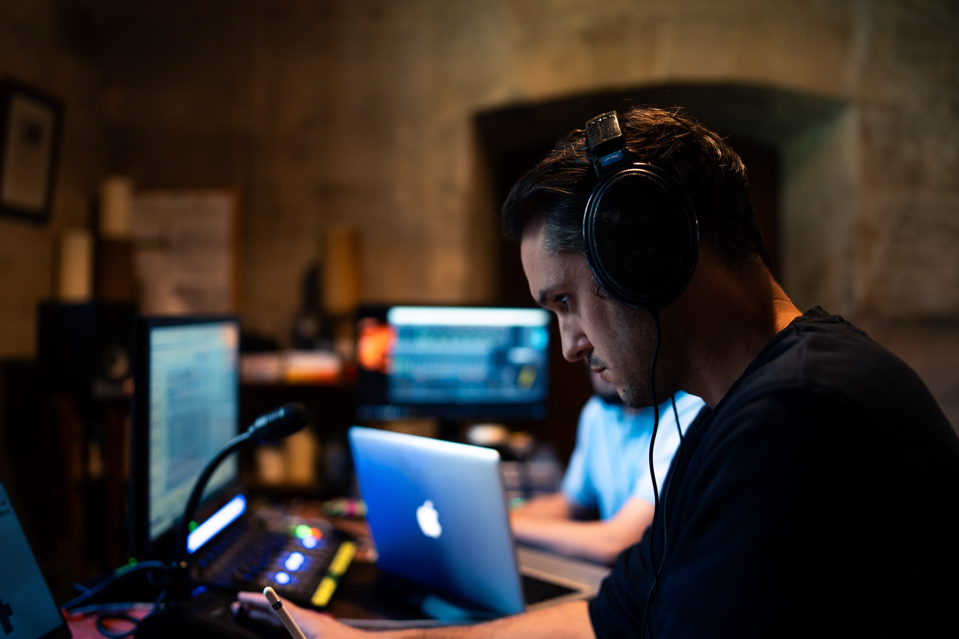 A man wearing headphones working at a mixing desk and laptop in a recording studio