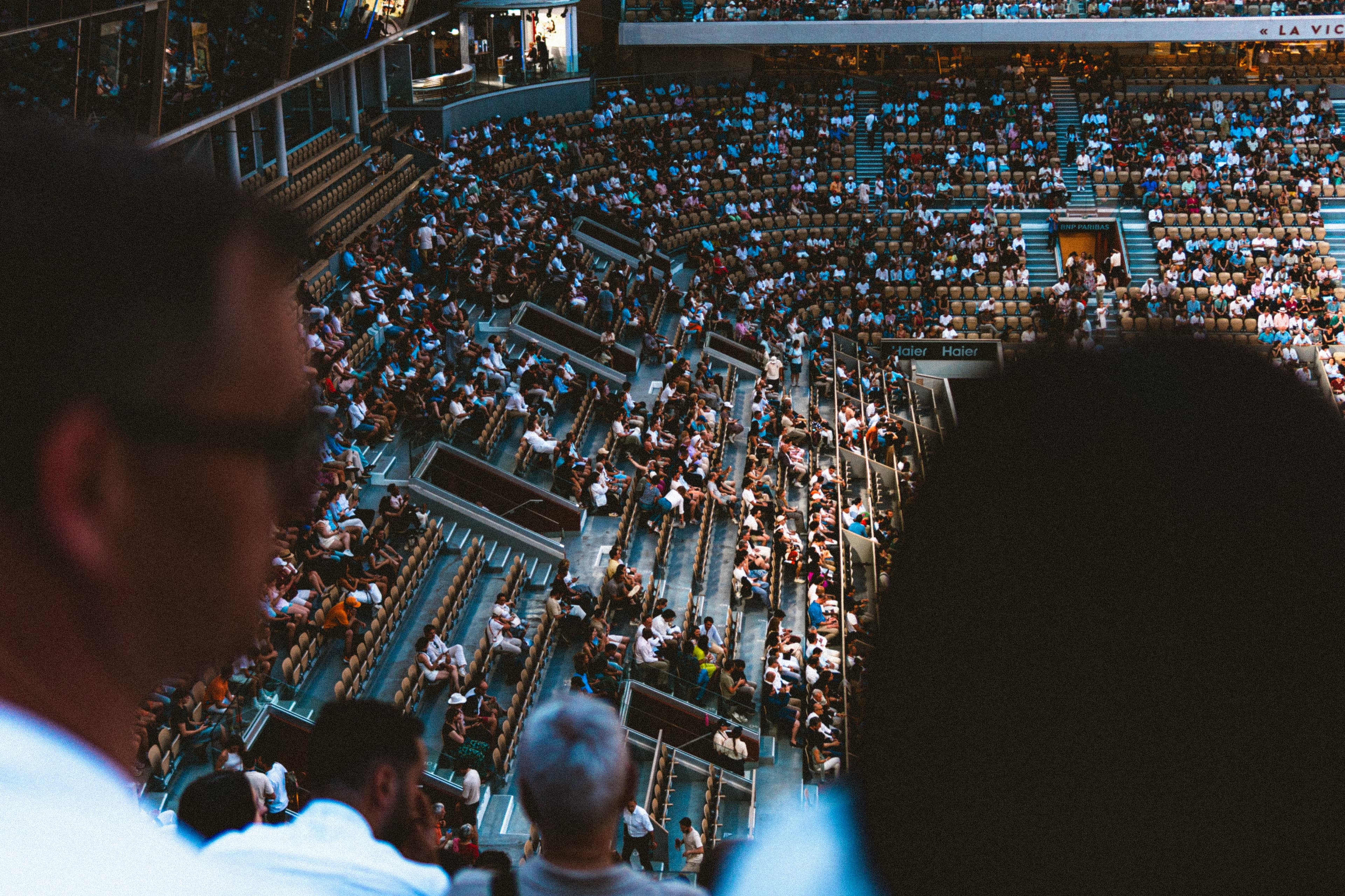 Silhouetted spectators looking out over a sunlit stadium crowd at Roland Garros