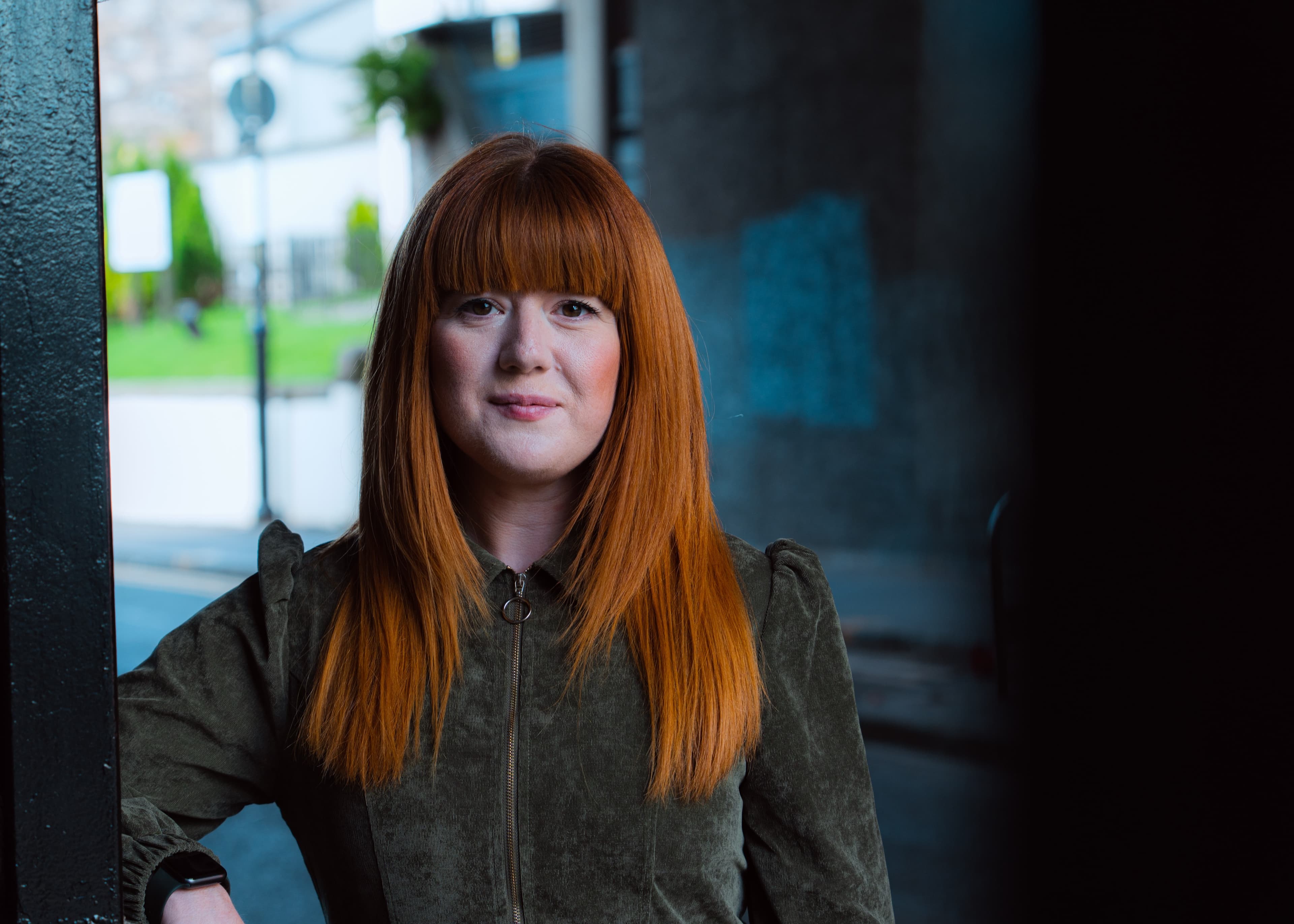A portrait of a woman with red hair and a green corduroy jacket, softly lit on a city street