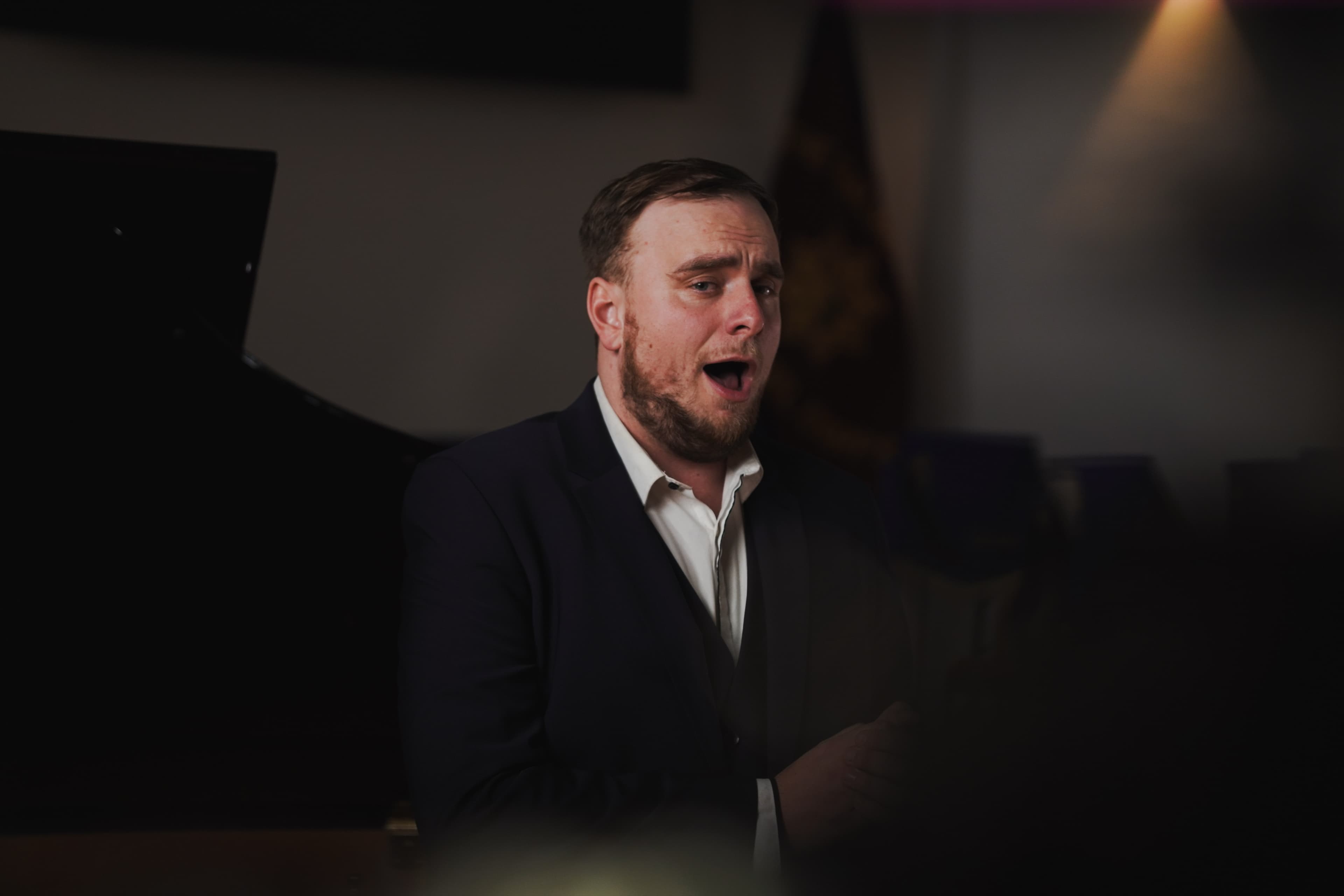 A tenor singing with mouth open in a dimly lit recital room