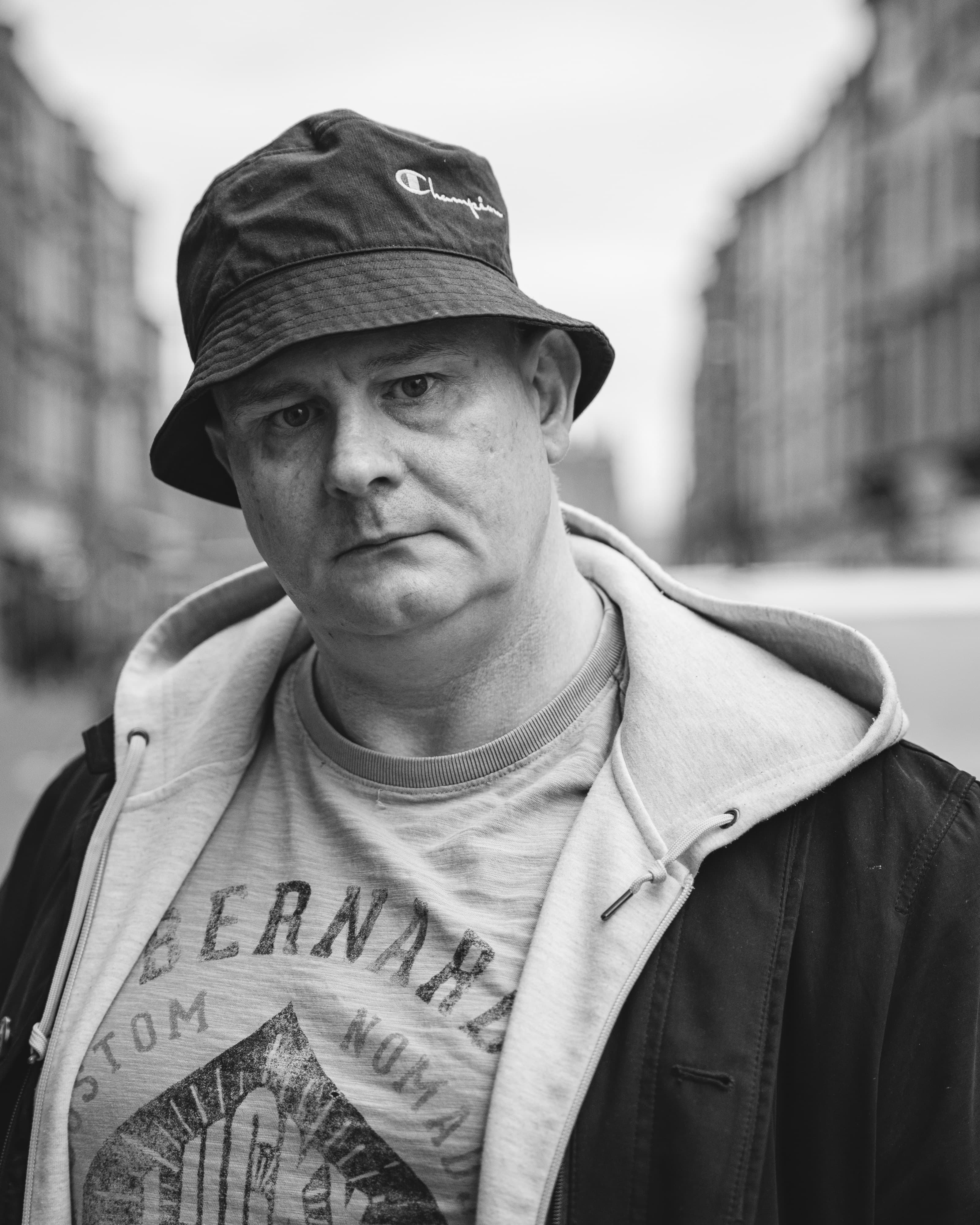 A close black and white portrait of a man in a bucket hat and hoodie on a city street