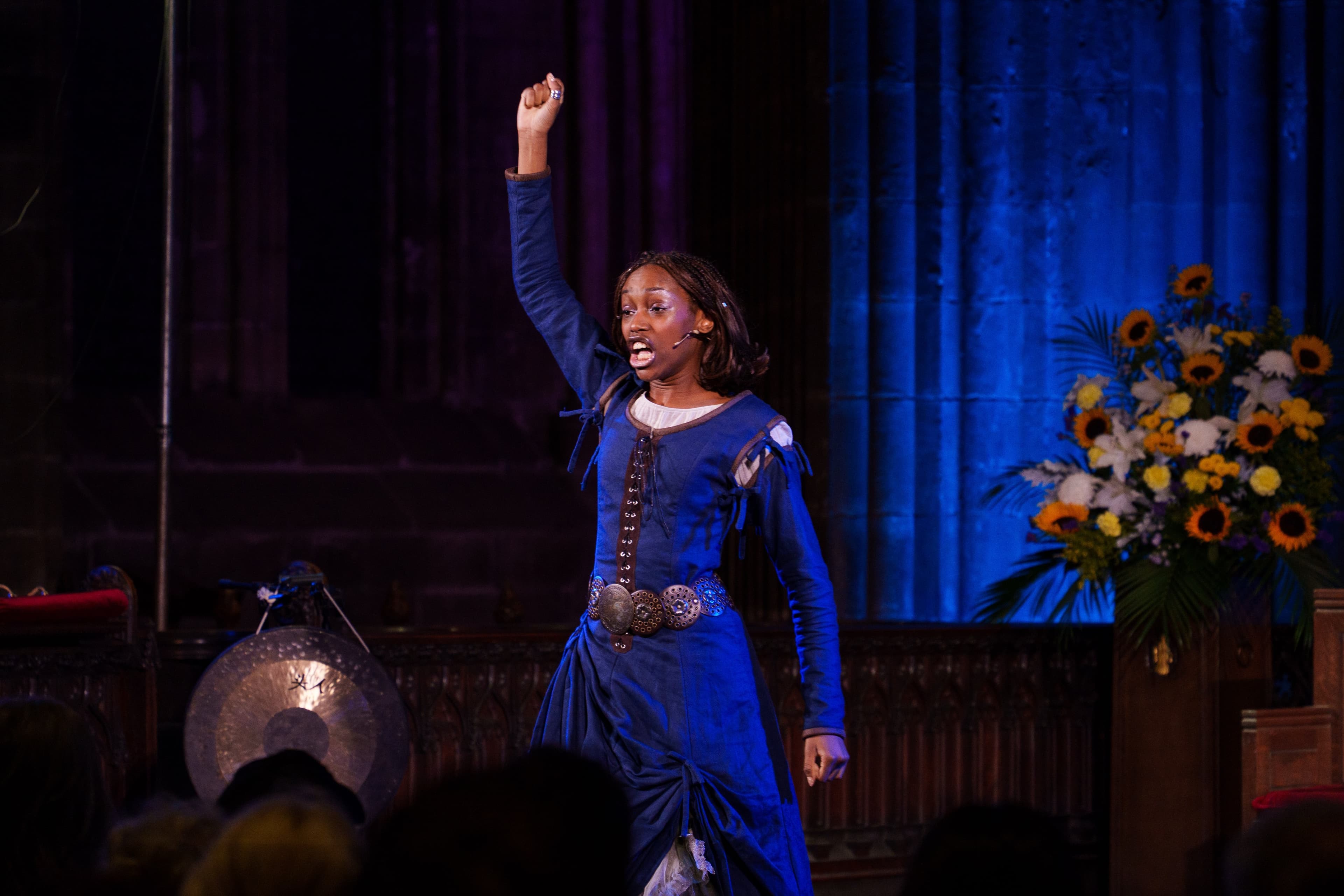 A performer in period costume raising a fist while singing on stage