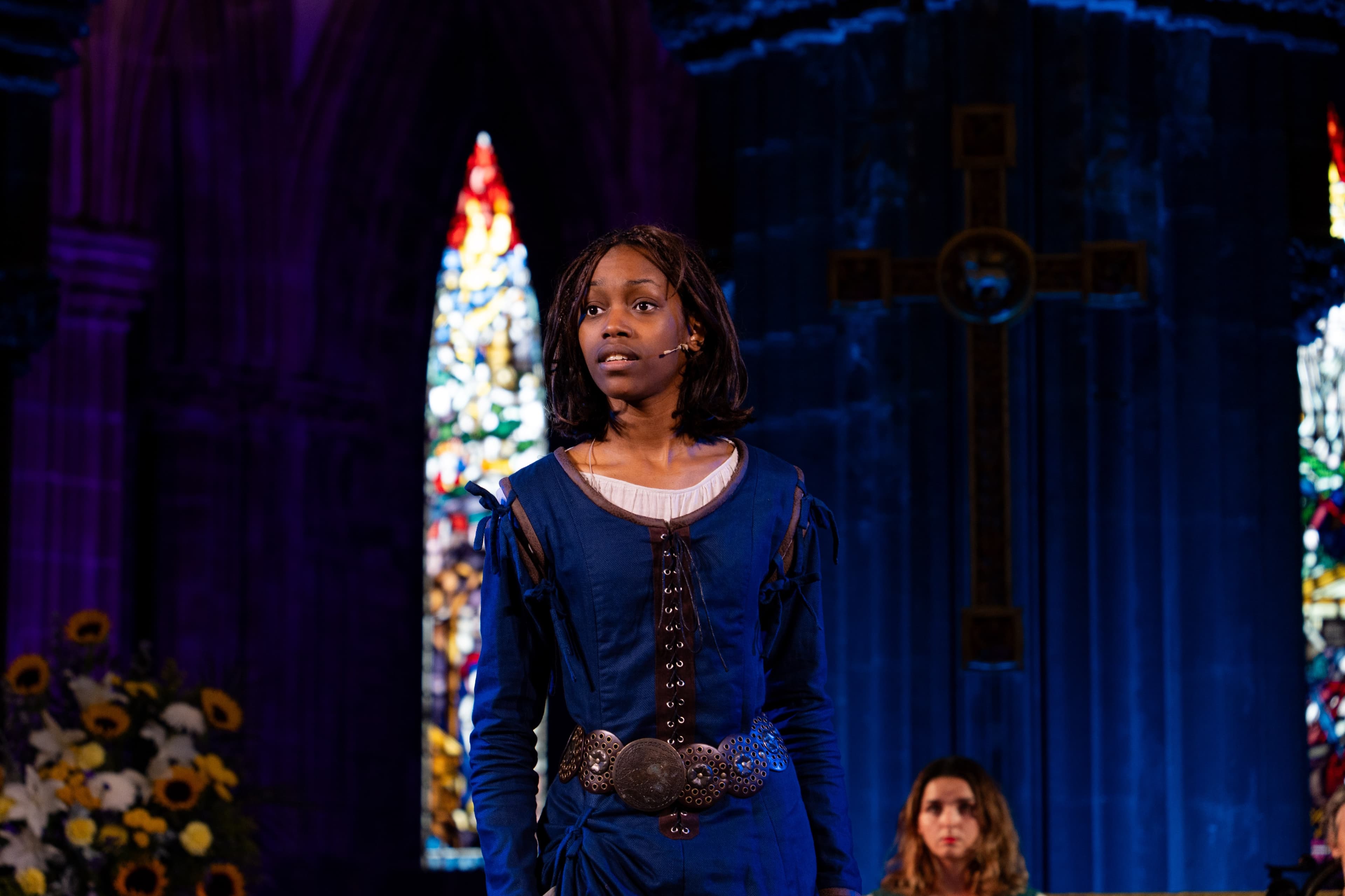 A performer in costume singing on stage in front of a stained glass window