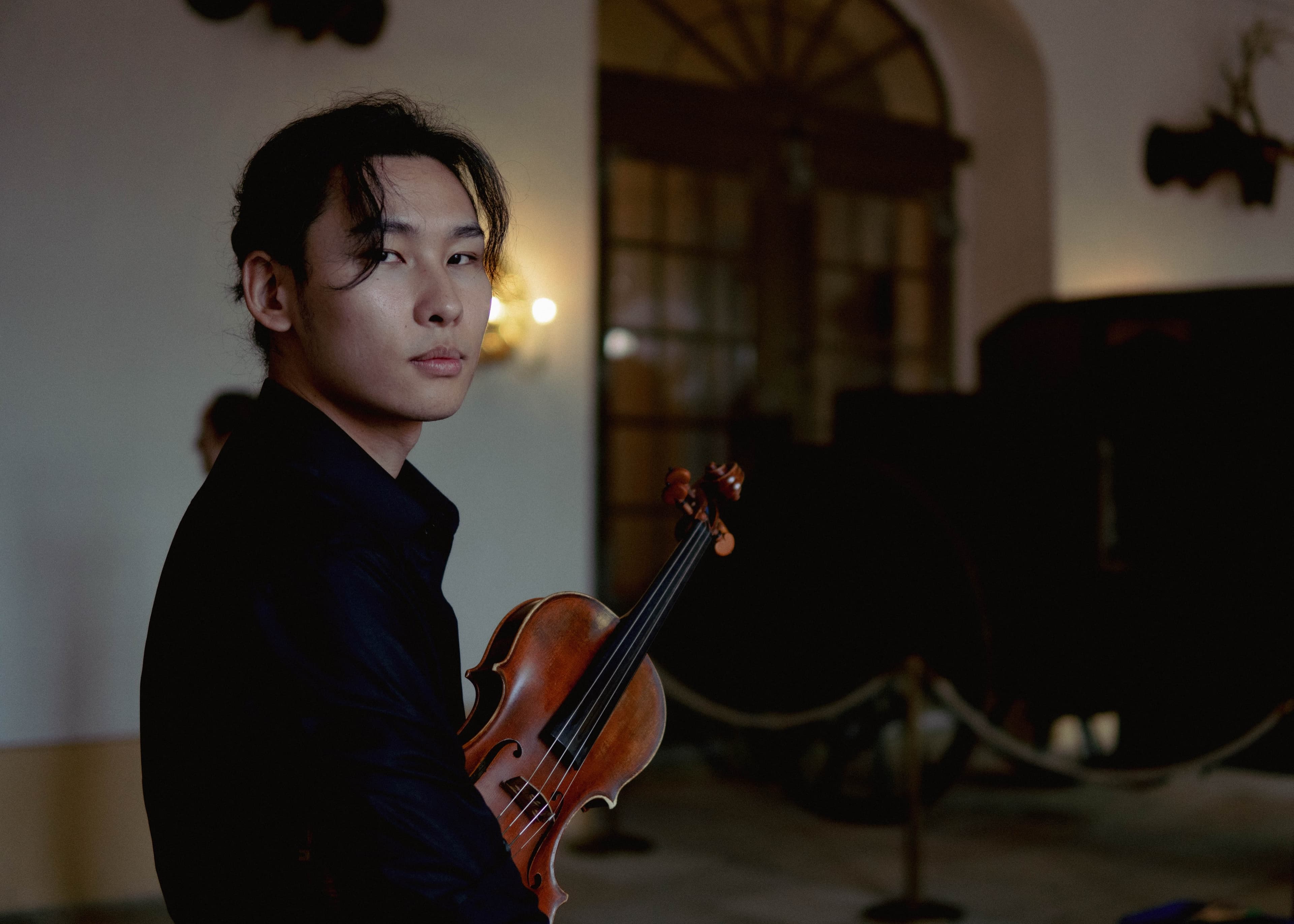 A violinist glancing back over his shoulder while holding his violin in a dimly lit hall